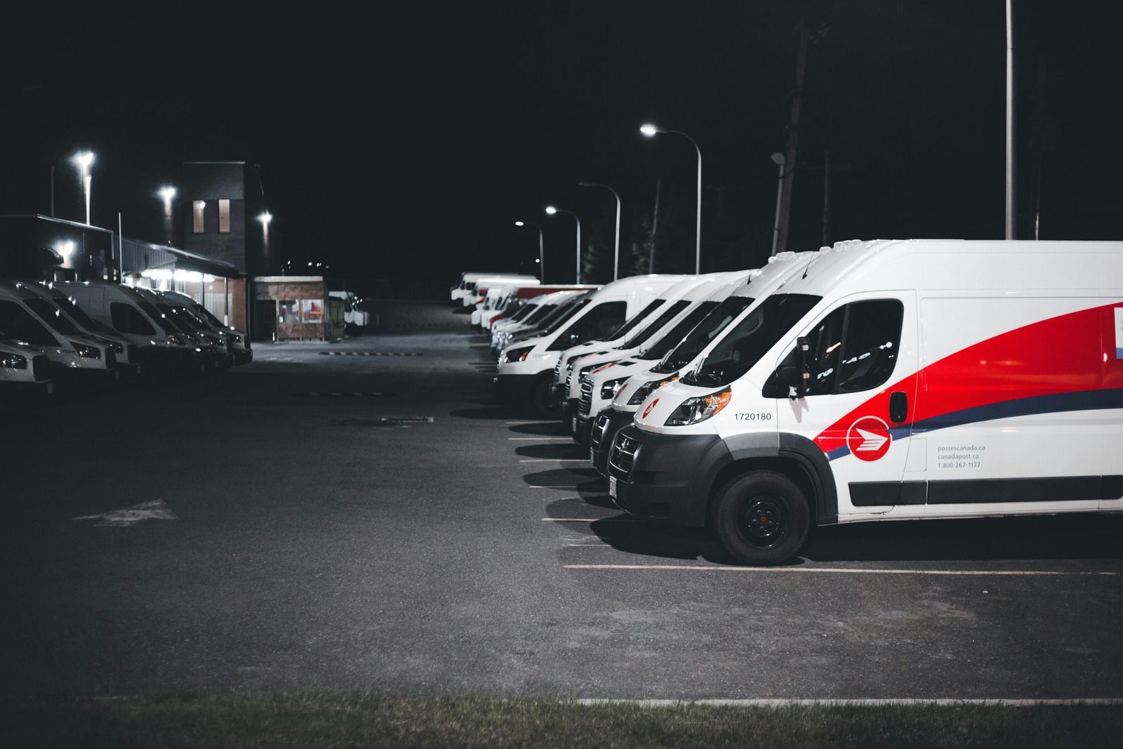 White delivery vans parked in a row at night under streetlights. Red and blue logo on the side.