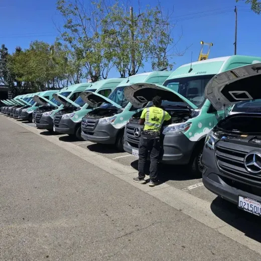 A row of green work vans with open hoods and a worker inspecting them in a parking lot
