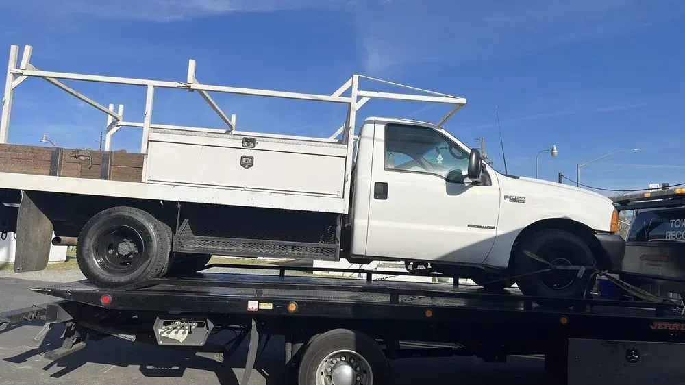 White utility truck strapped on a flatbed tow truck under a blue sky.