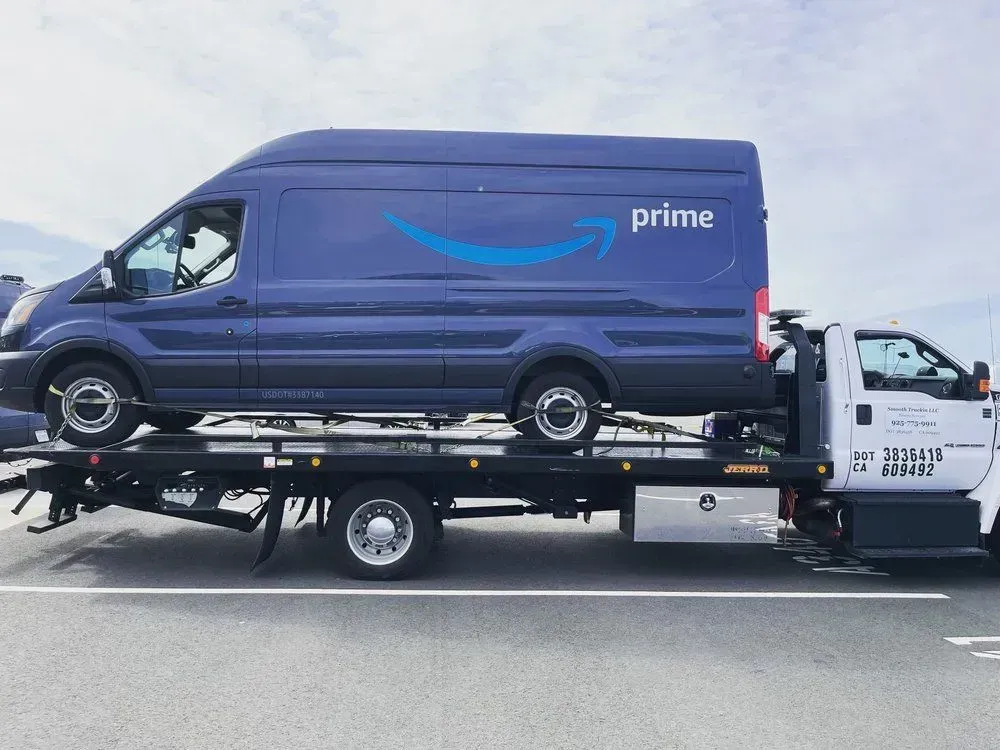 Purple Amazon Prime van loaded on a white tow truck on a road.