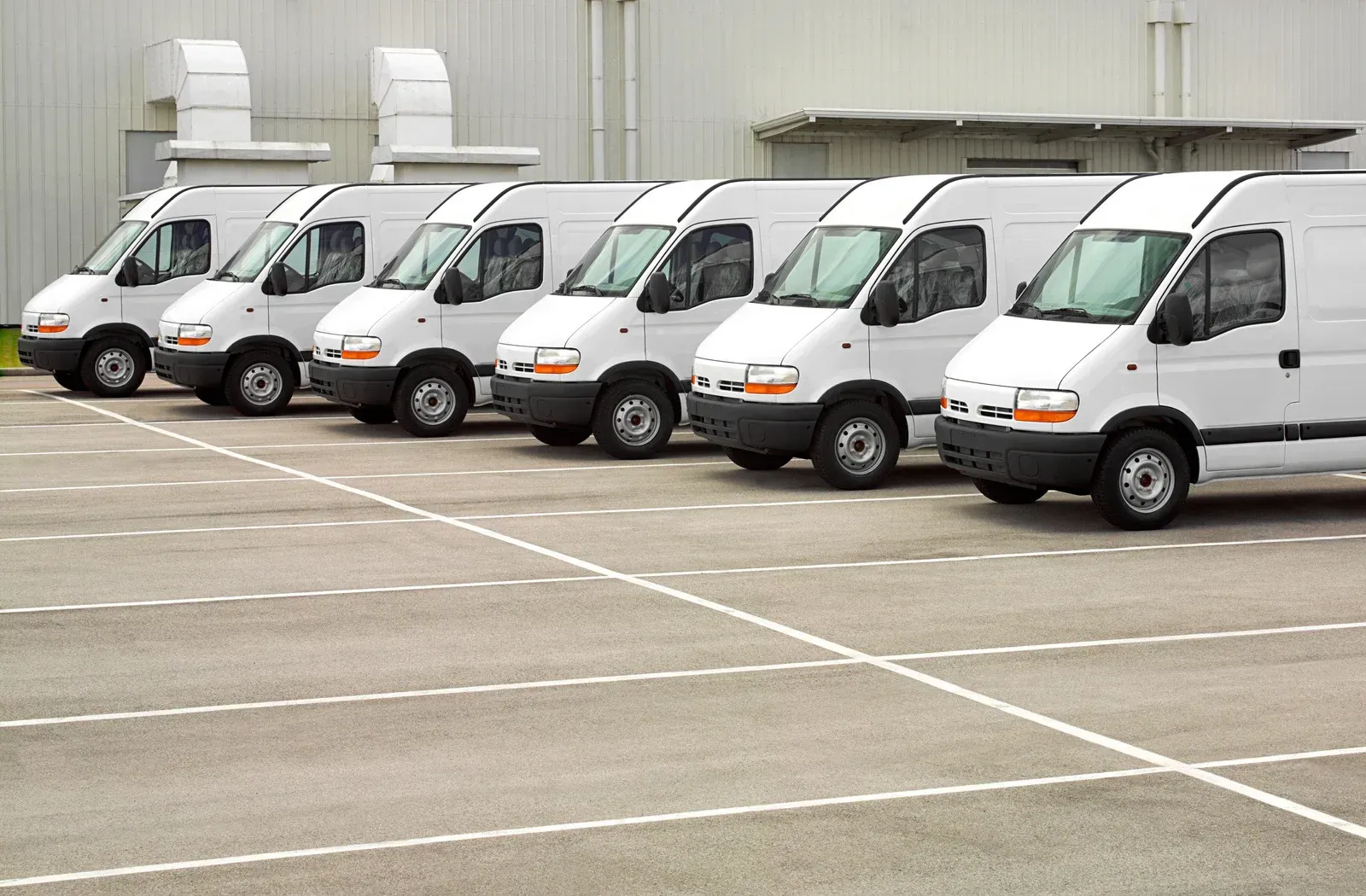 Six white fleet vans parked in a row outside for inspection