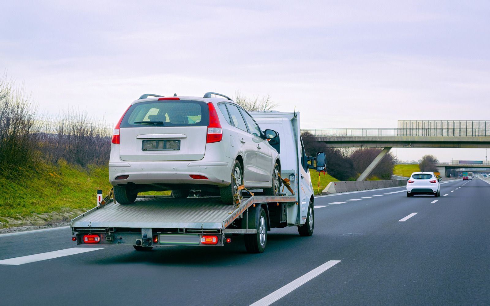 Car carrying a white SUV on a highway, with another car ahead and an overpass in the distance