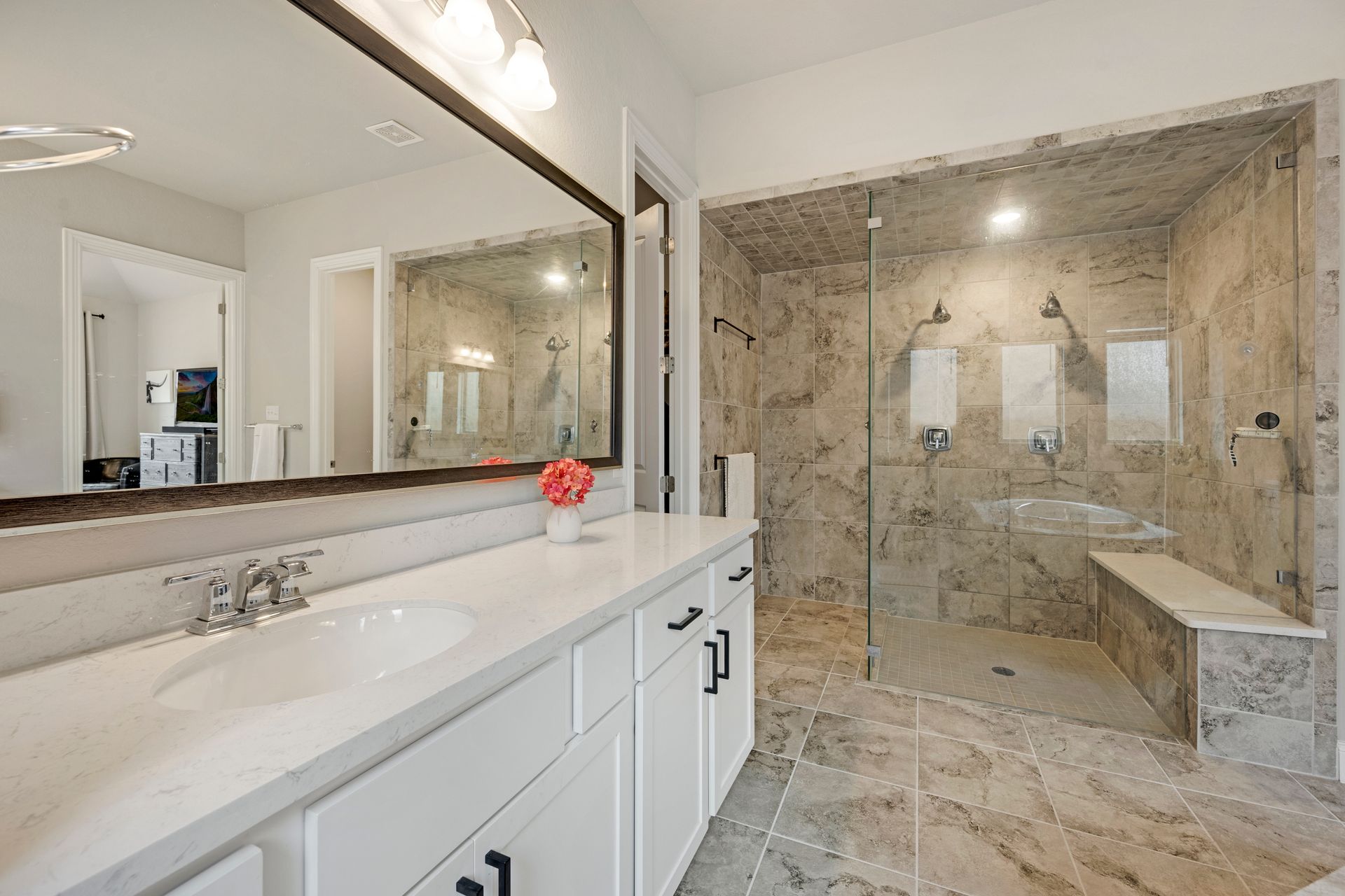 A modern bathroom with a white vanity, large mirror, and a walk-in stone shower with a built-in bench.