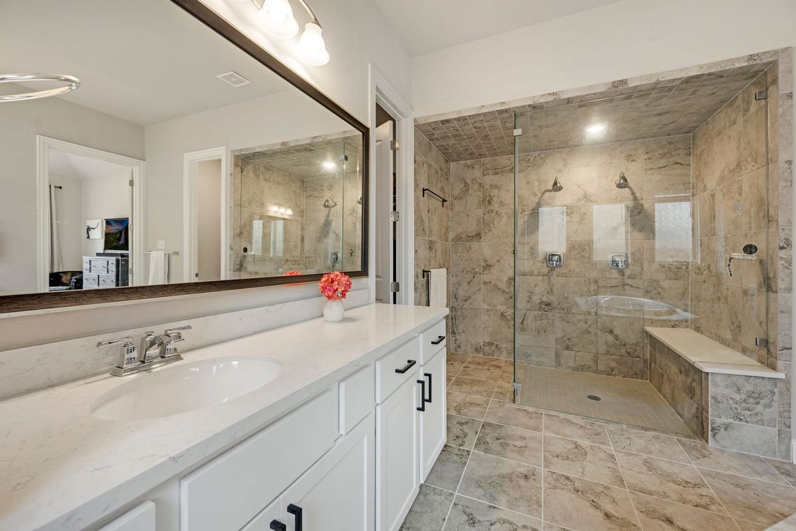 A modern bathroom featuring a white vanity with a marble countertop, a large mirror, and a spacious walk-in stone shower.