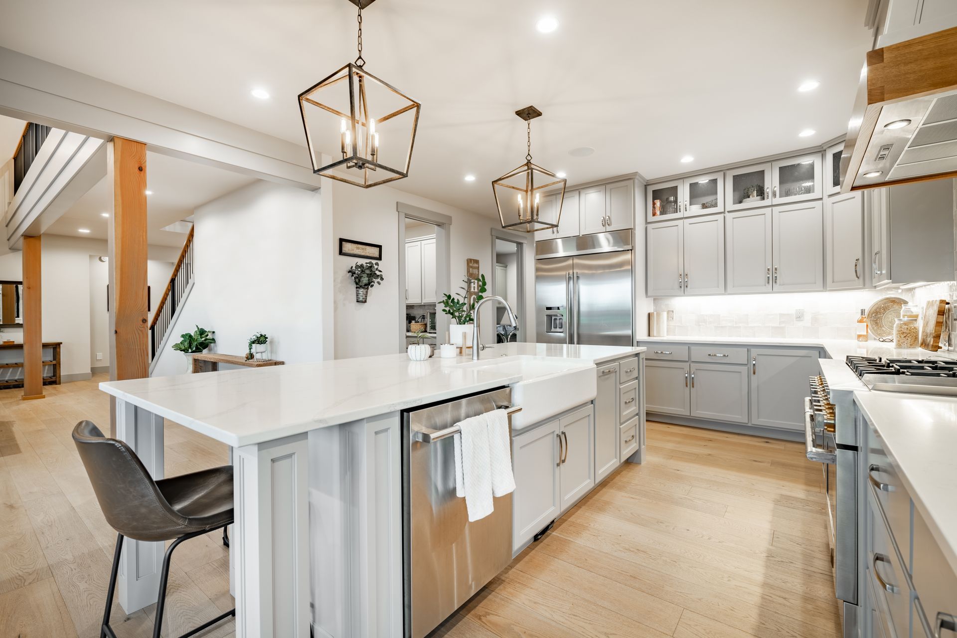 Modern kitchen featuring a large white island, light gray cabinetry, stainless steel appliances, and wood flooring.