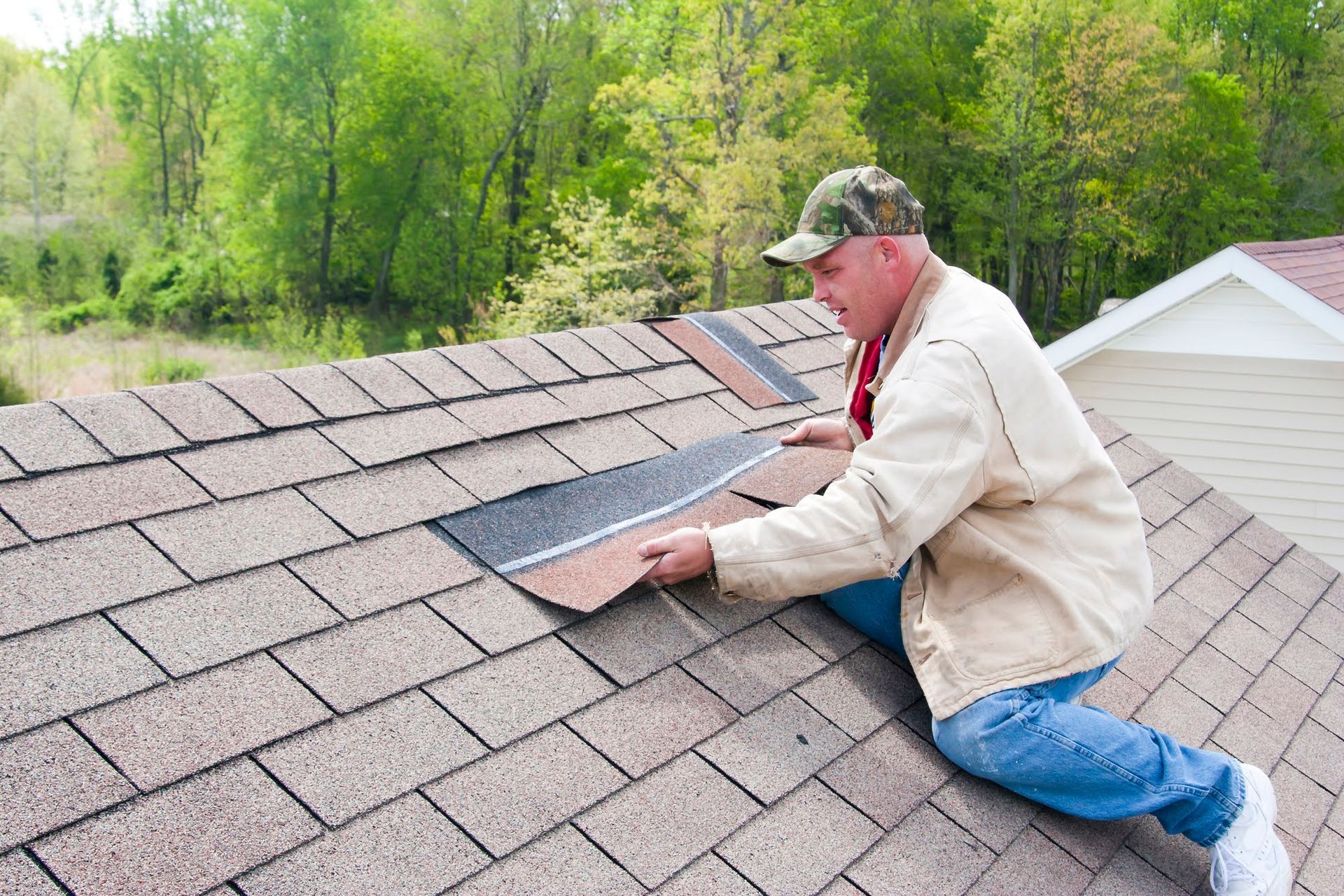 Man on a roof replacing shingles, holding a brown shingle above the roof.