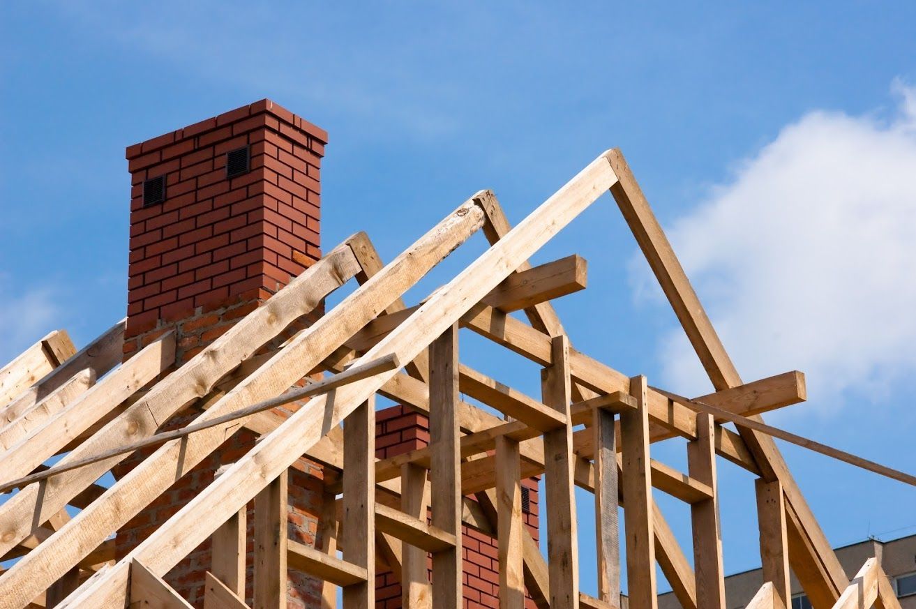Wooden roof framing with brick chimney against a blue sky.