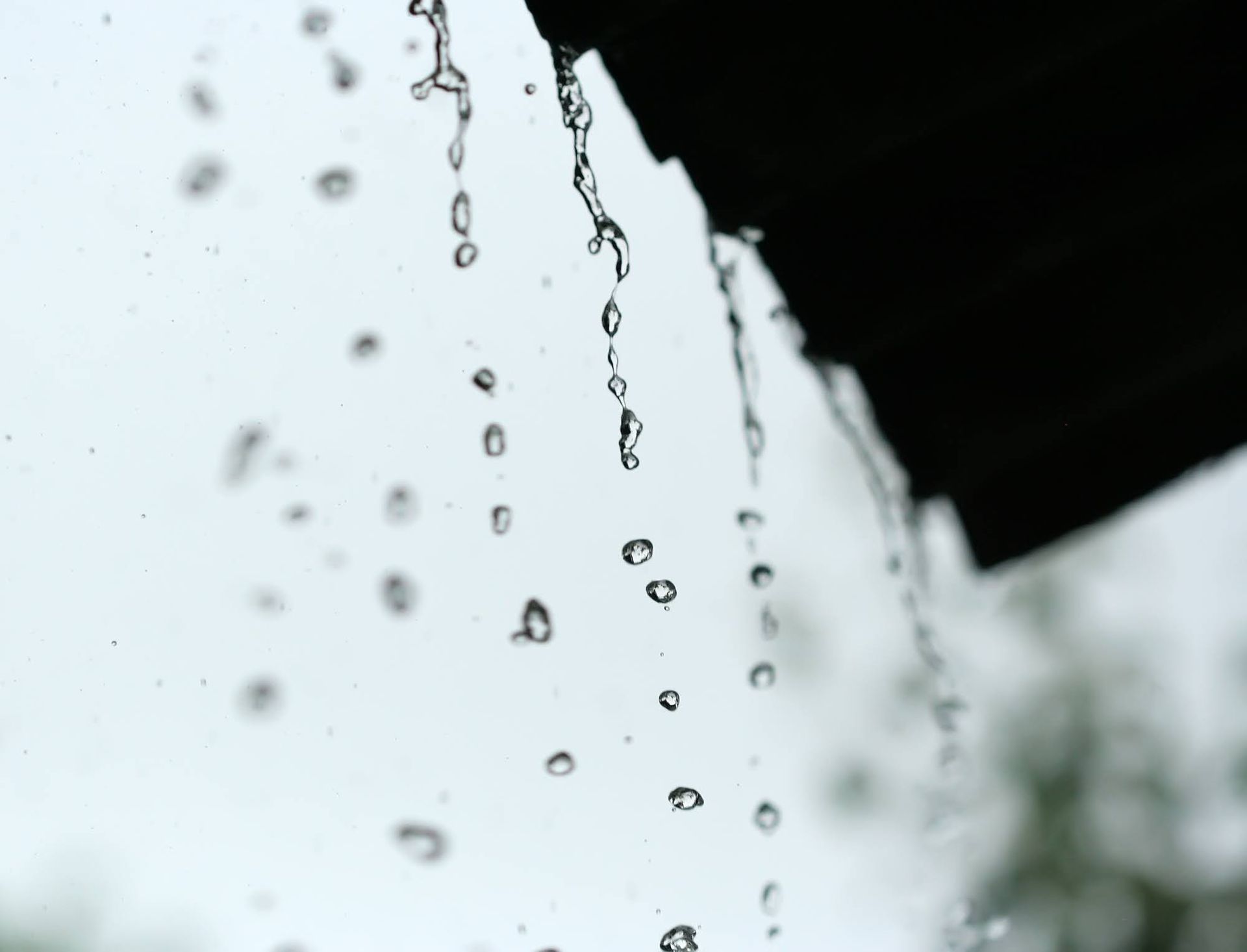 Raindrops falling from a roof against a gray sky.
