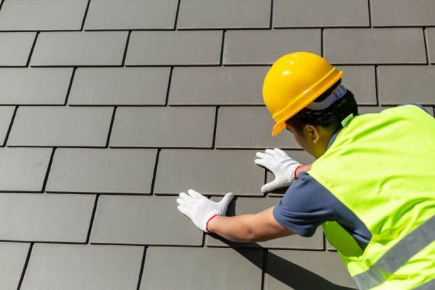 Worker in yellow hard hat and vest installing gray tiles on a wall.