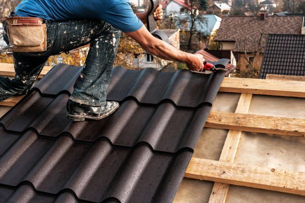 Roofer installing dark brown metal roof tiles on a wooden structure.
