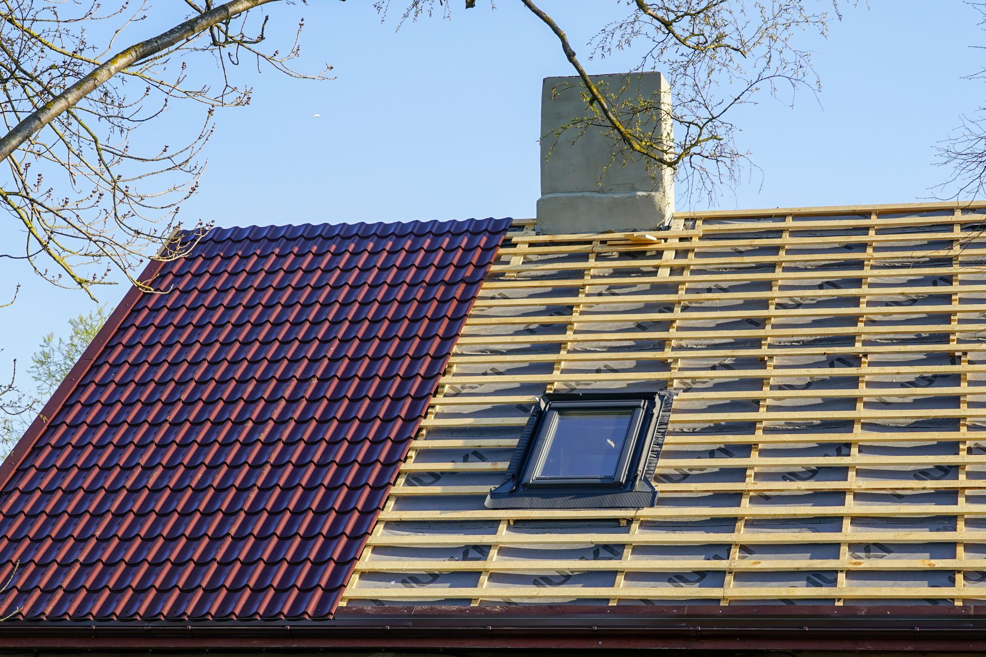 Roof partially covered with red tiles, showing construction with exposed wooden beams and a chimney.