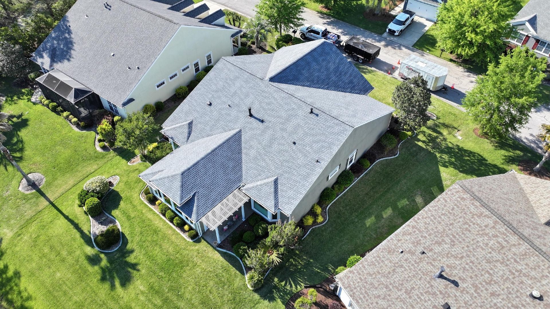 Aerial view of a white multi-roof house with gray shingles and metal accents, surrounded by a yard with green landscaping. Aerial view of a white multi-roof house with gray shingles and metal accents, surrounded by a yard with green landscaping.