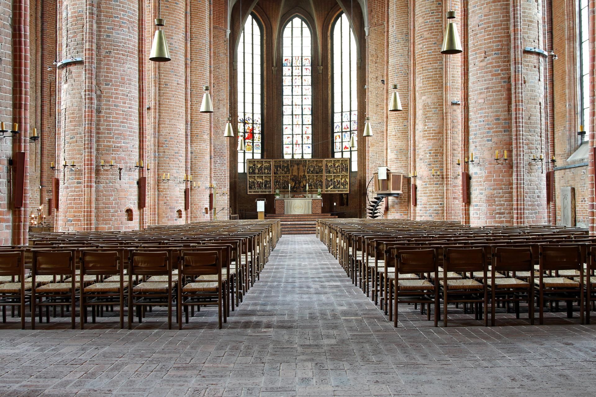 Rows of chairs face an altar inside a brick church with arched windows.