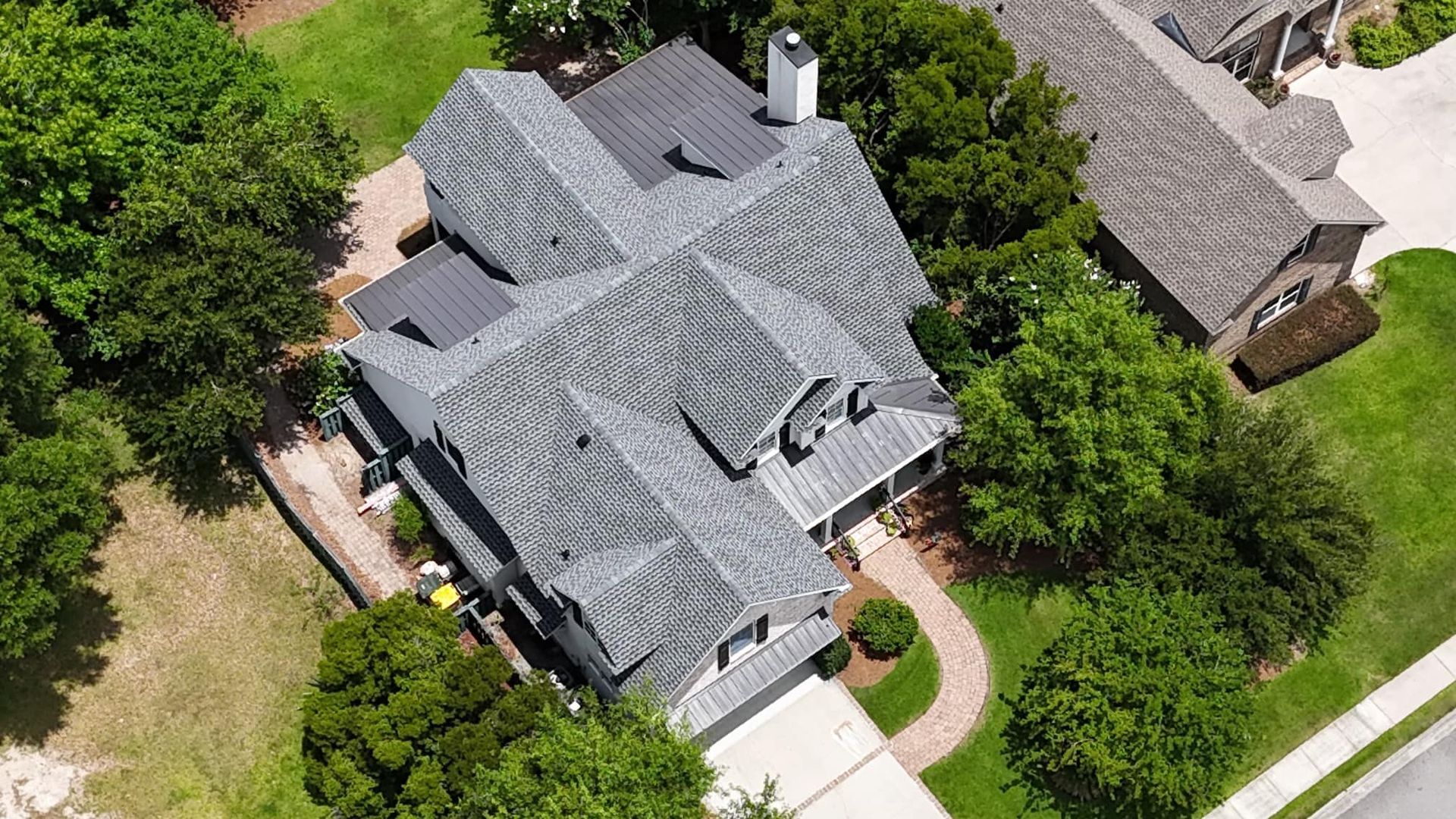 Aerial view of a gray-roofed house surrounded by trees, with a brick pathway leading to the front door.