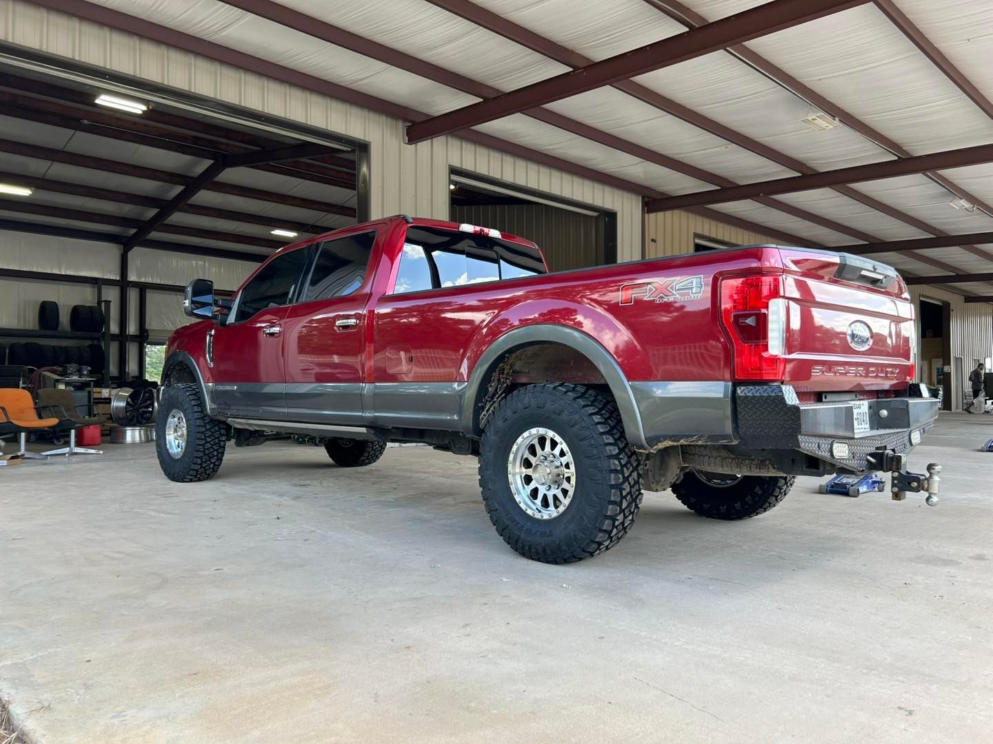 Red lifted pickup truck parked inside a large metal garage with open sides