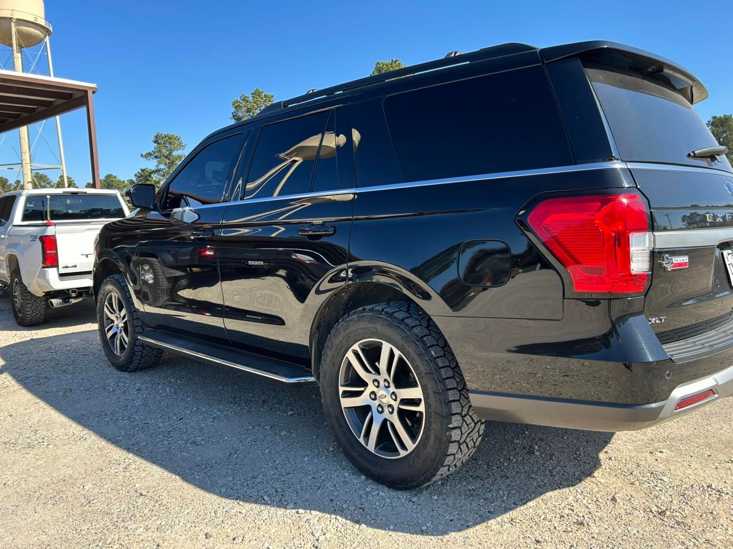 Black SUV parked on a gravel lot beside a white pickup truck under a clear sky
