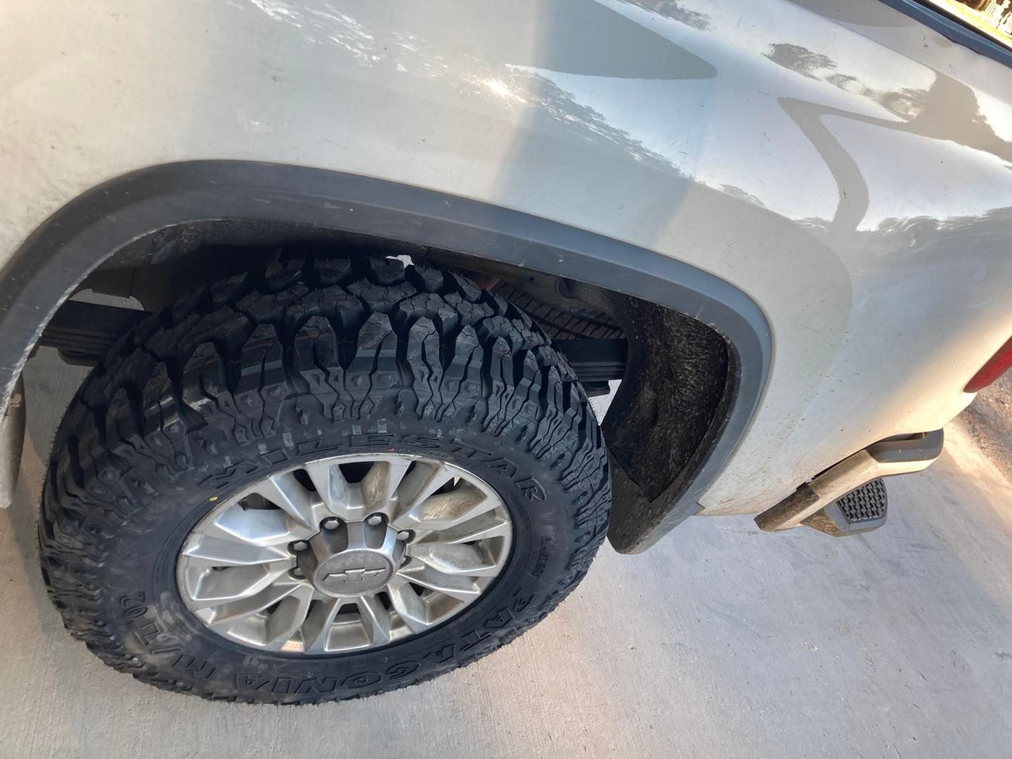 Close-up of a silver SUV’s rear wheel and tire on pavement.