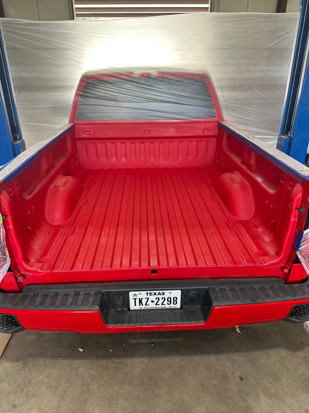Red pickup truck bed with red tailgate open inside a garage, rear view.