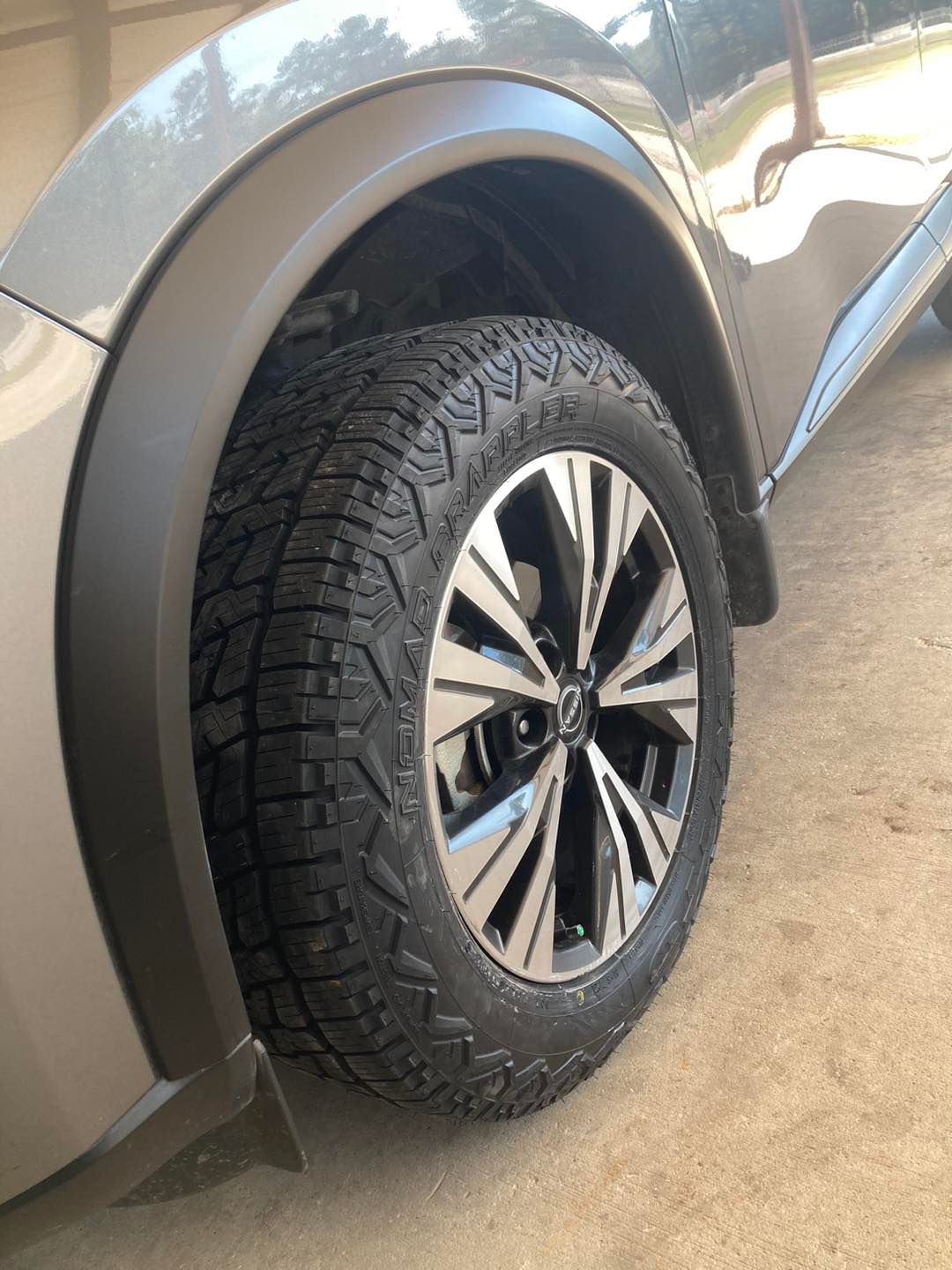 Close-up of a silver SUV’s front wheel and tire on a wet pavement.