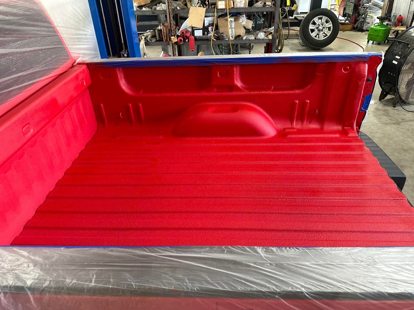 Red pickup truck bed freshly painted glossy red, shown in a workshop.