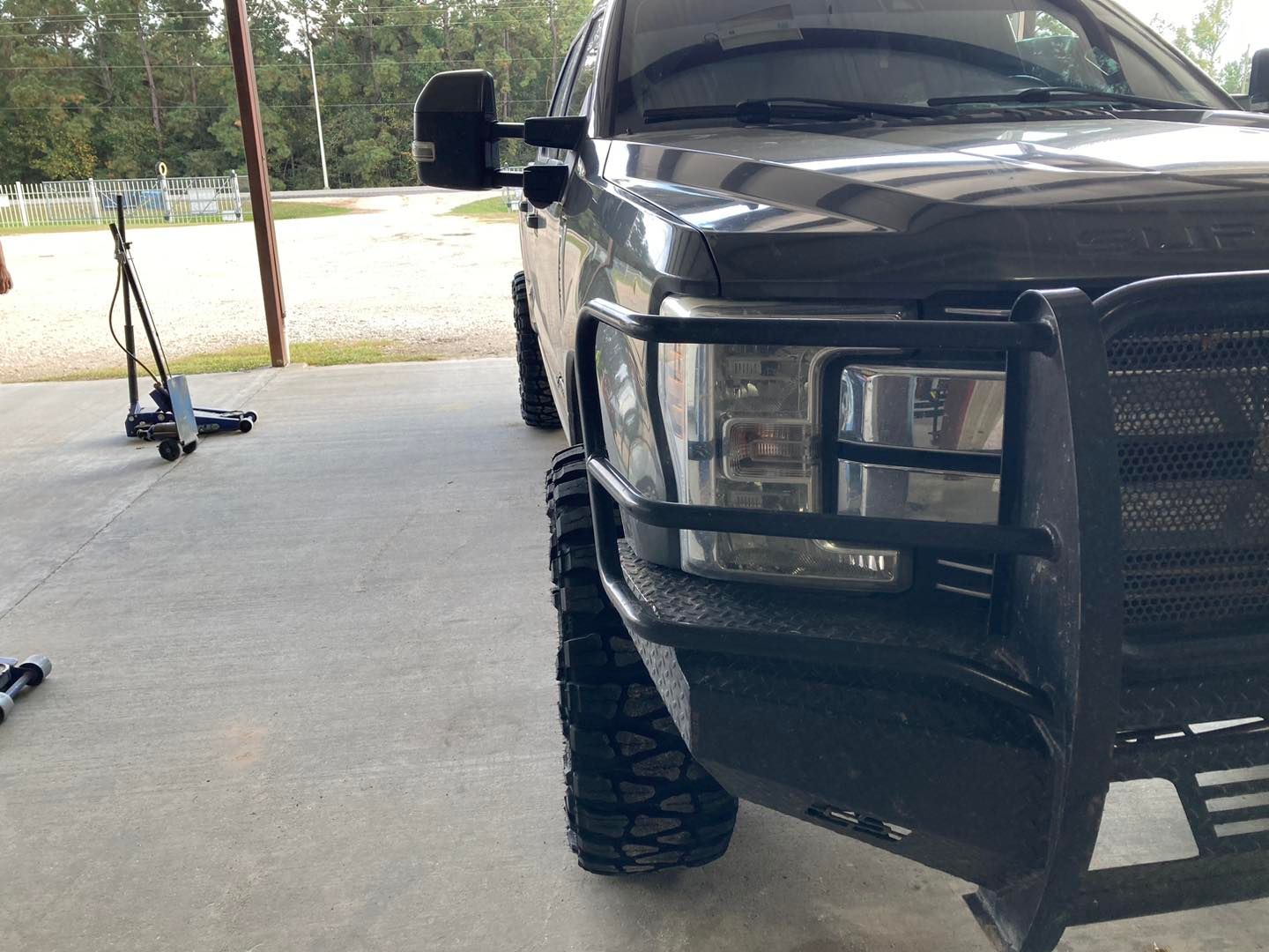 Black pickup truck parked in a driveway, with a lifted front tire and a tow truck in the background.