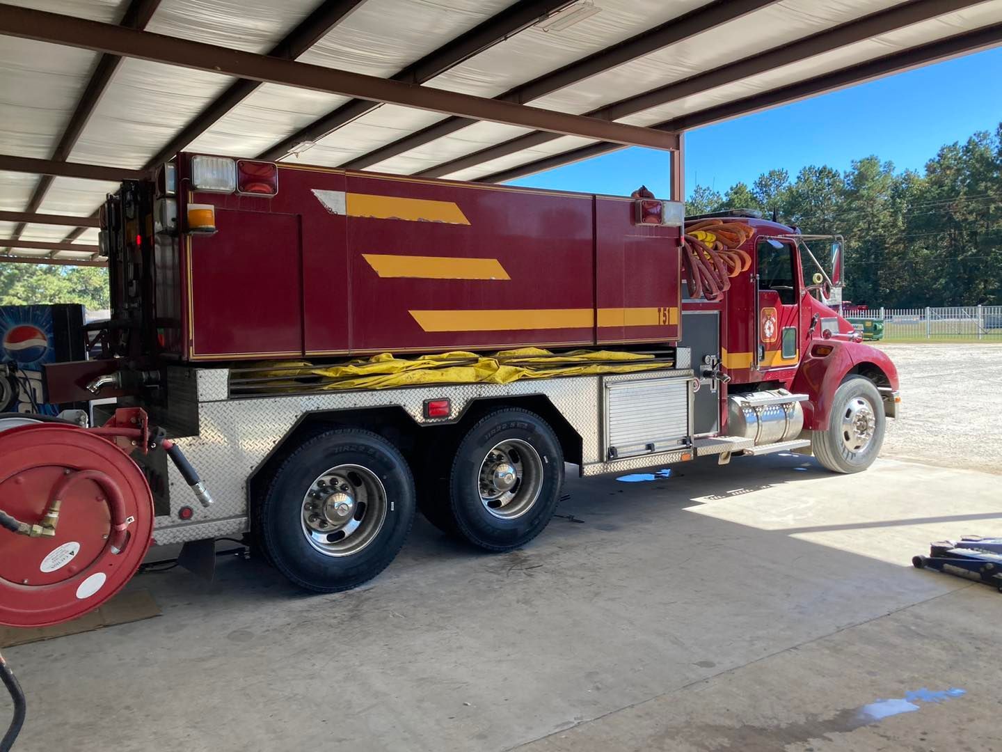 Red and gold fire truck parked under a metal shelter, side view.