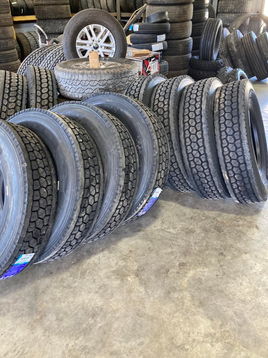 Stacks of new black car tires in a warehouse, with a few wheels and tires leaning against the wall.