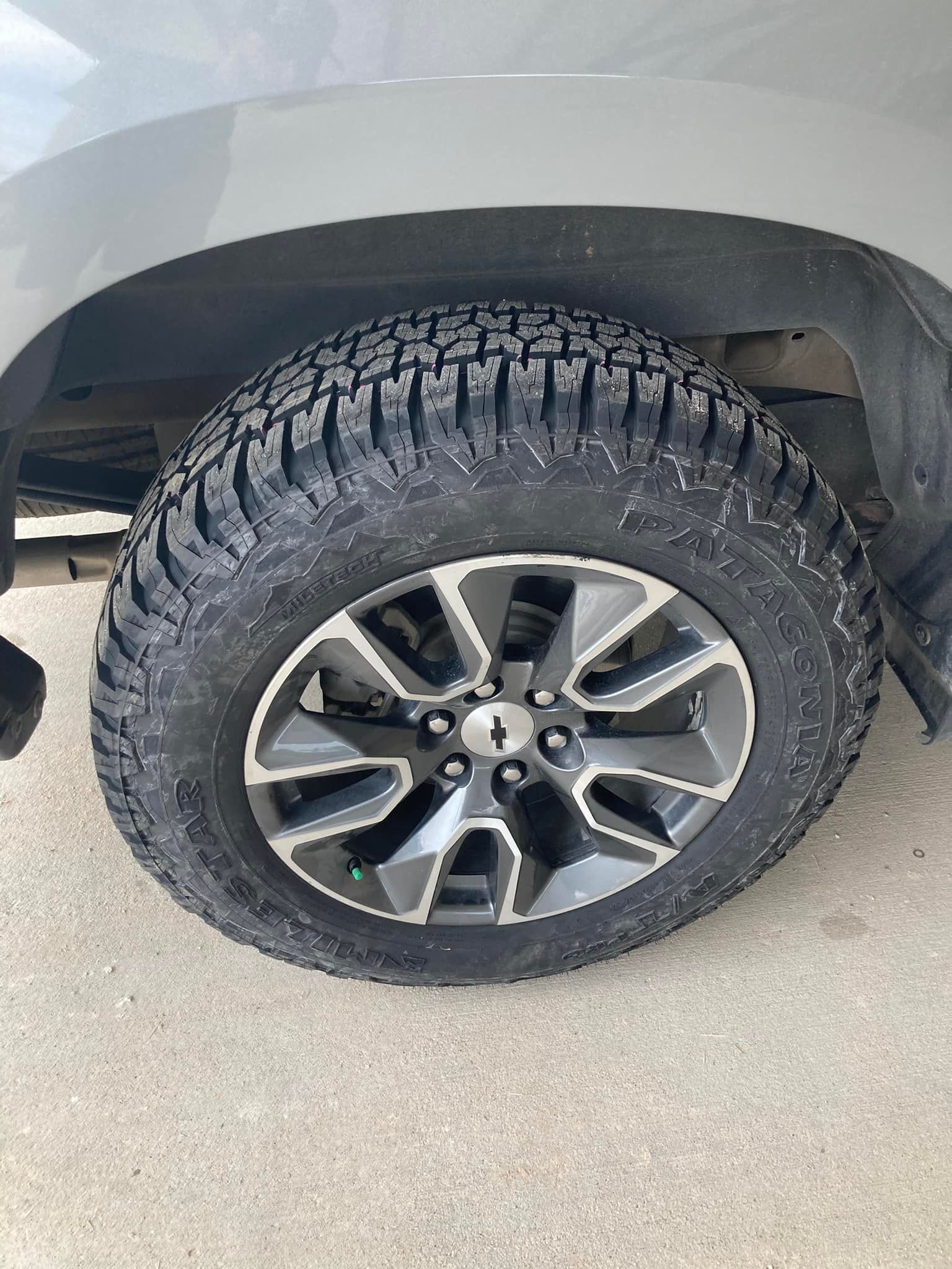 Close-up of a truck’s off-road tire and alloy wheel beneath a gray fender.
