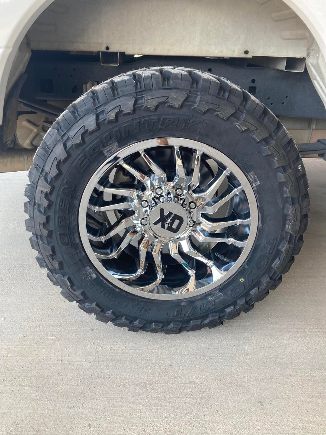 Lifted truck with large knobby tire and chrome XD wheel parked on concrete.