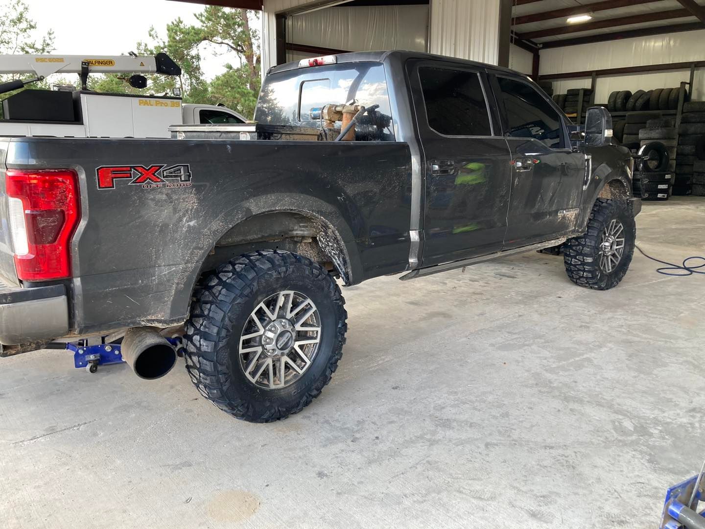Black lifted Ford F-150 pickup parked in a garage, side view with off-road tires and large exhaust.