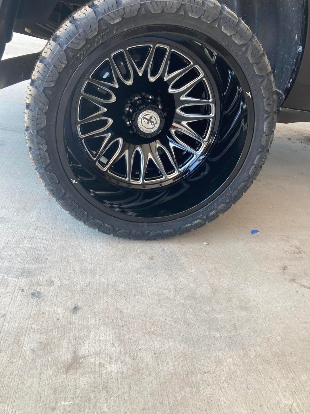 Black alloy wheel with large off-road tire on a concrete floor