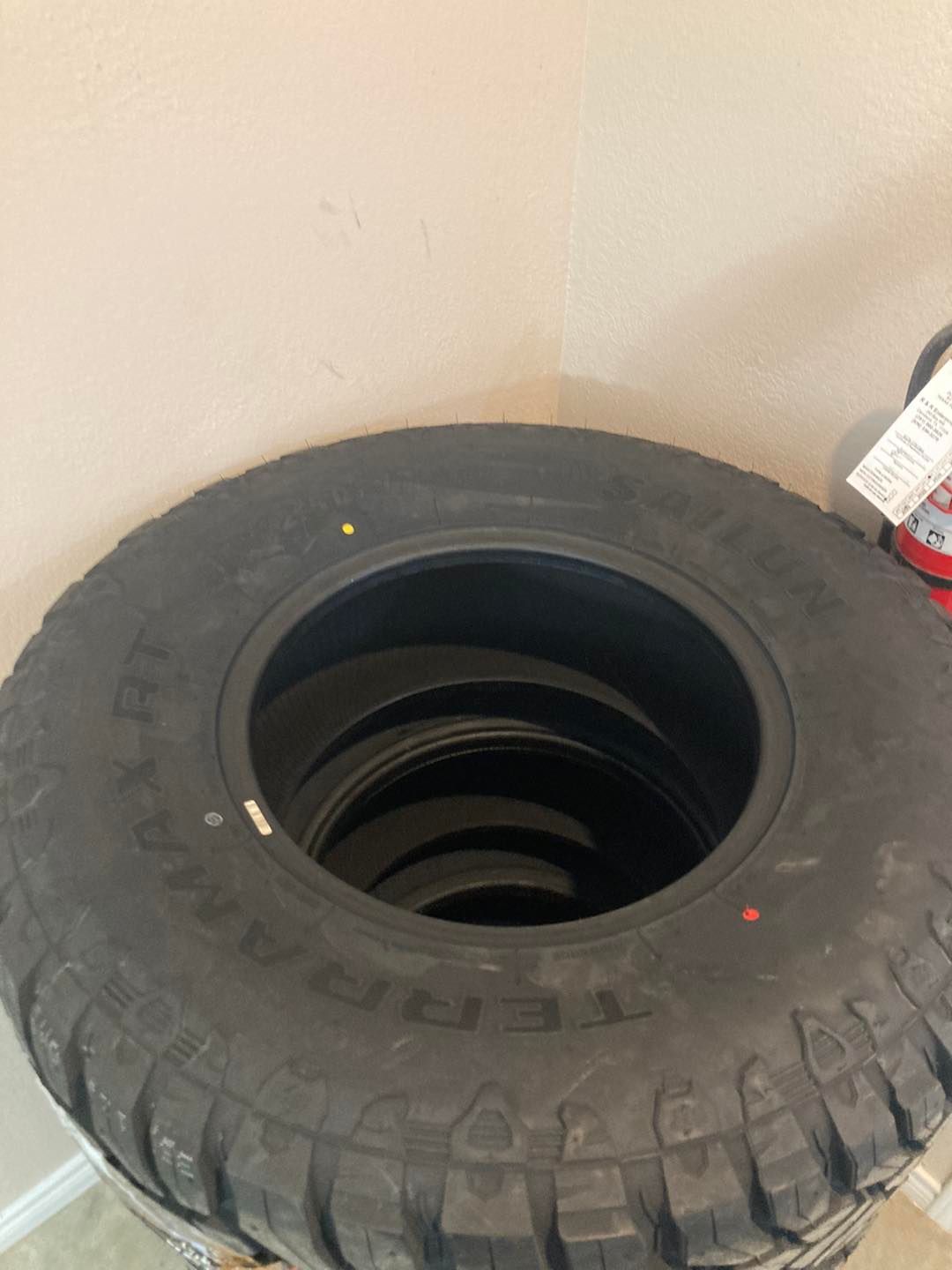 Large black tire standing upright in a corner, with smaller tires stacked inside it.