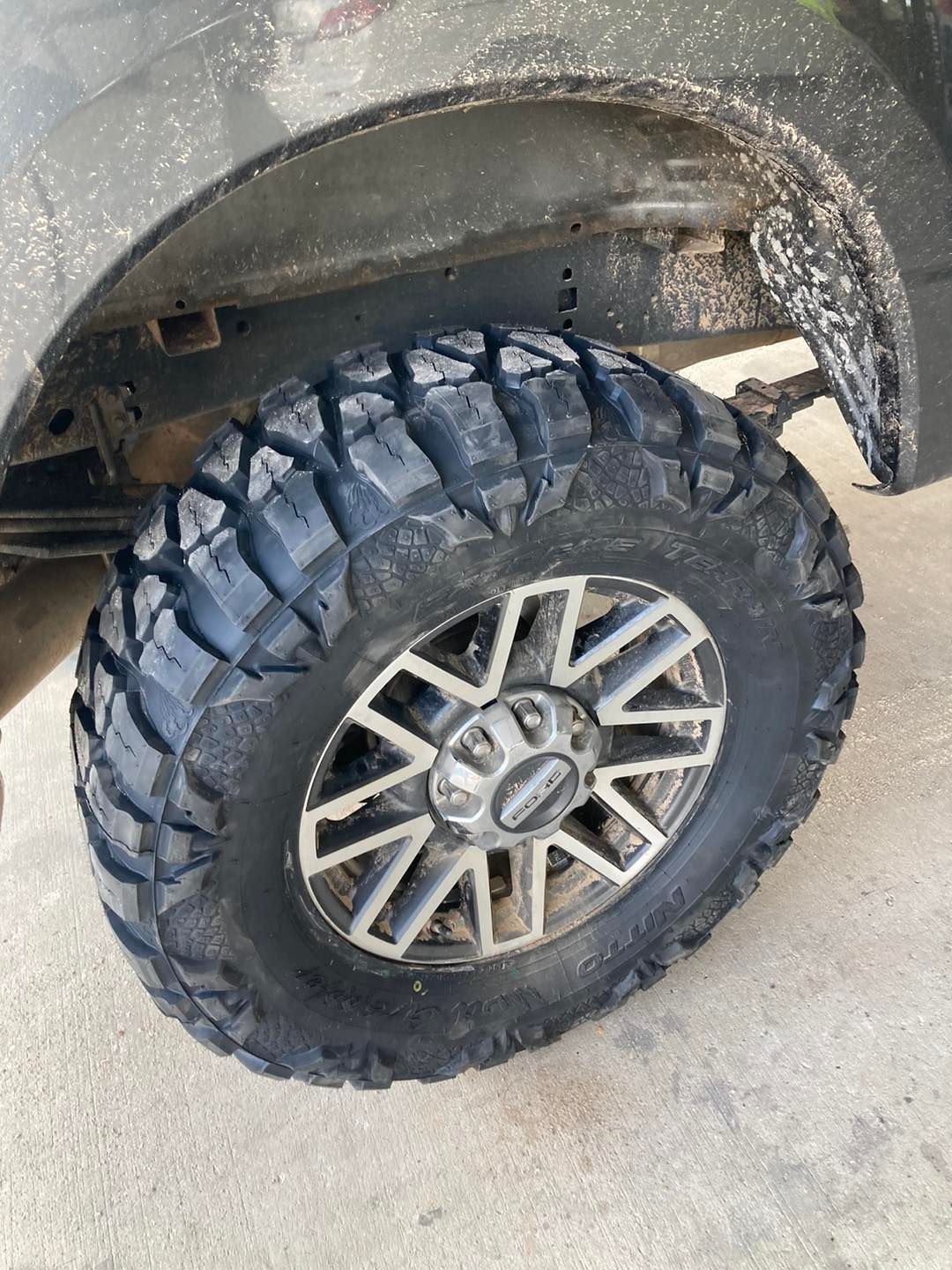 Close-up of a rugged off-road tire and alloy wheel under a dusty vehicle fender.