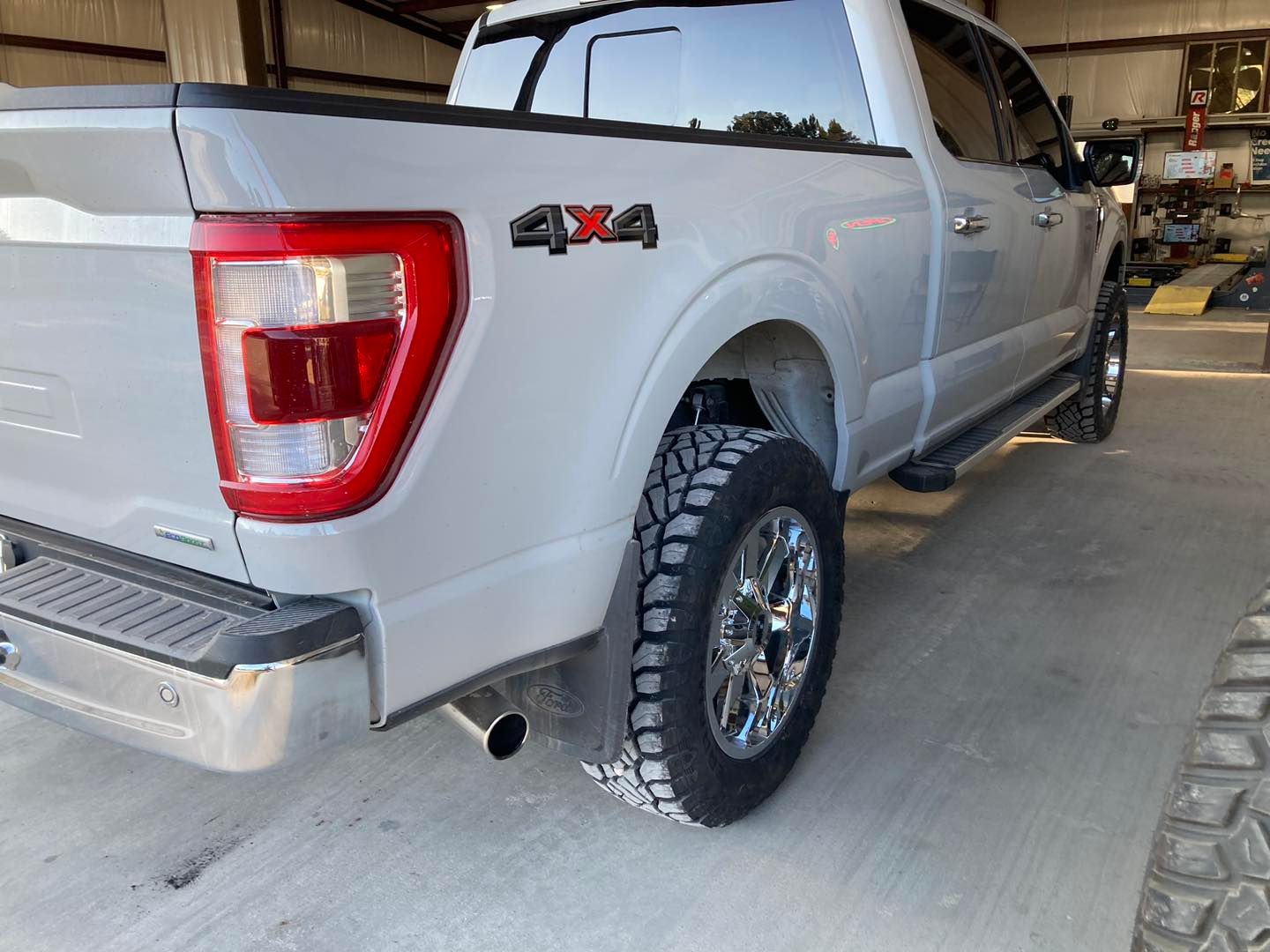 White 4x4 pickup truck parked indoors, rear side view with off-road tires and chrome wheels