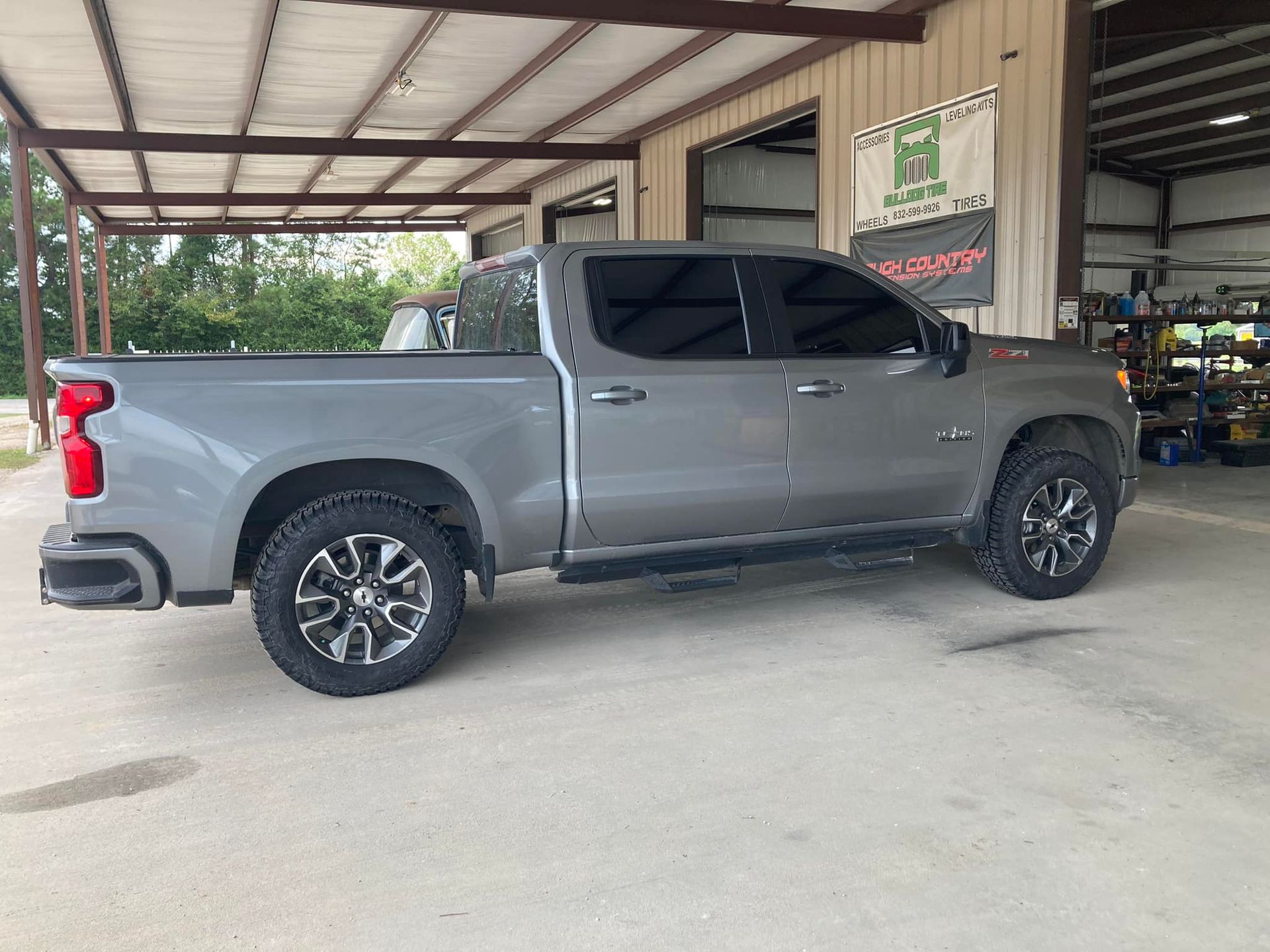 Silver pickup truck parked under a covered carport, side view.