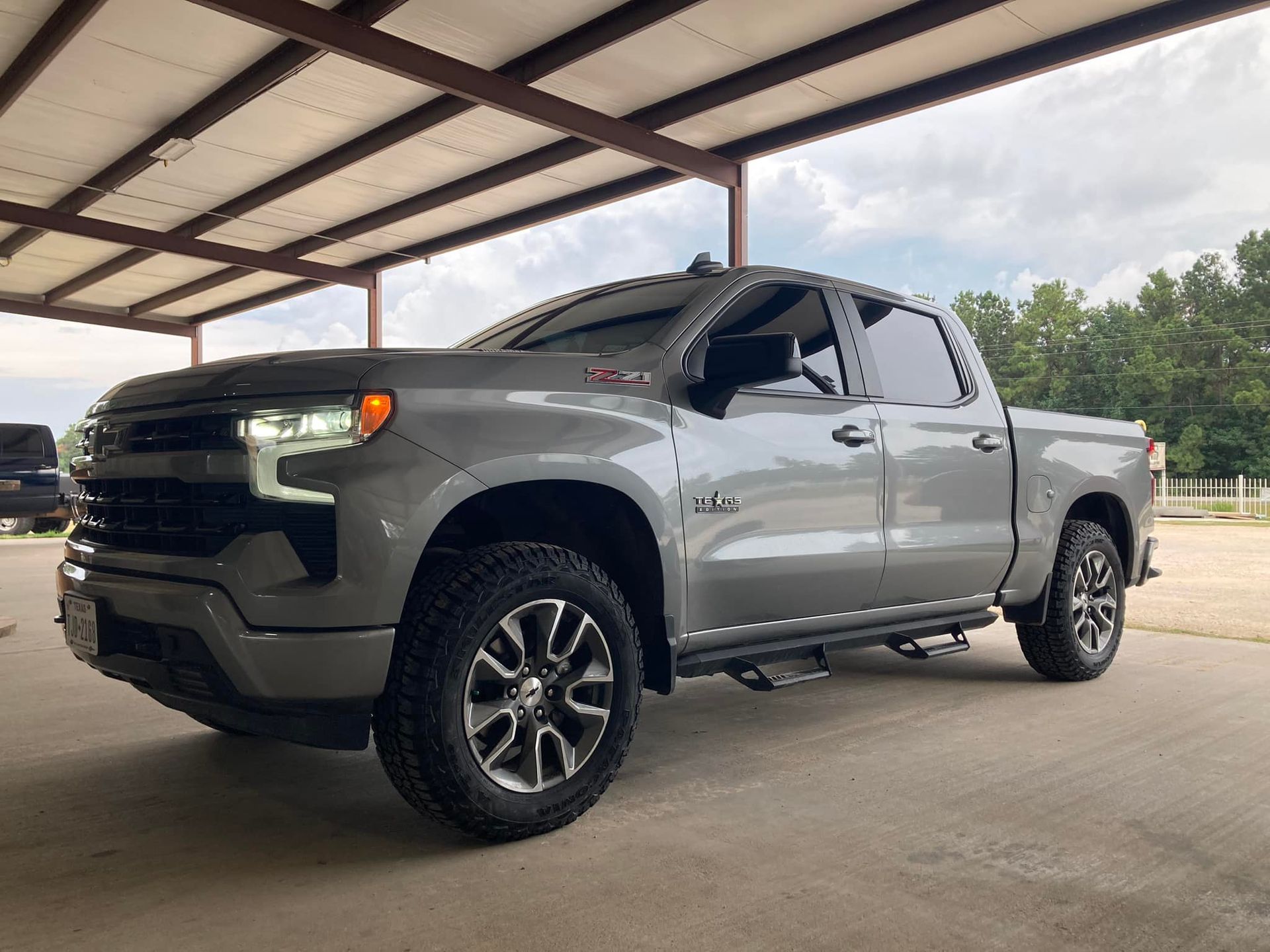 Silver pickup truck parked under a metal roof at an outdoor lot.