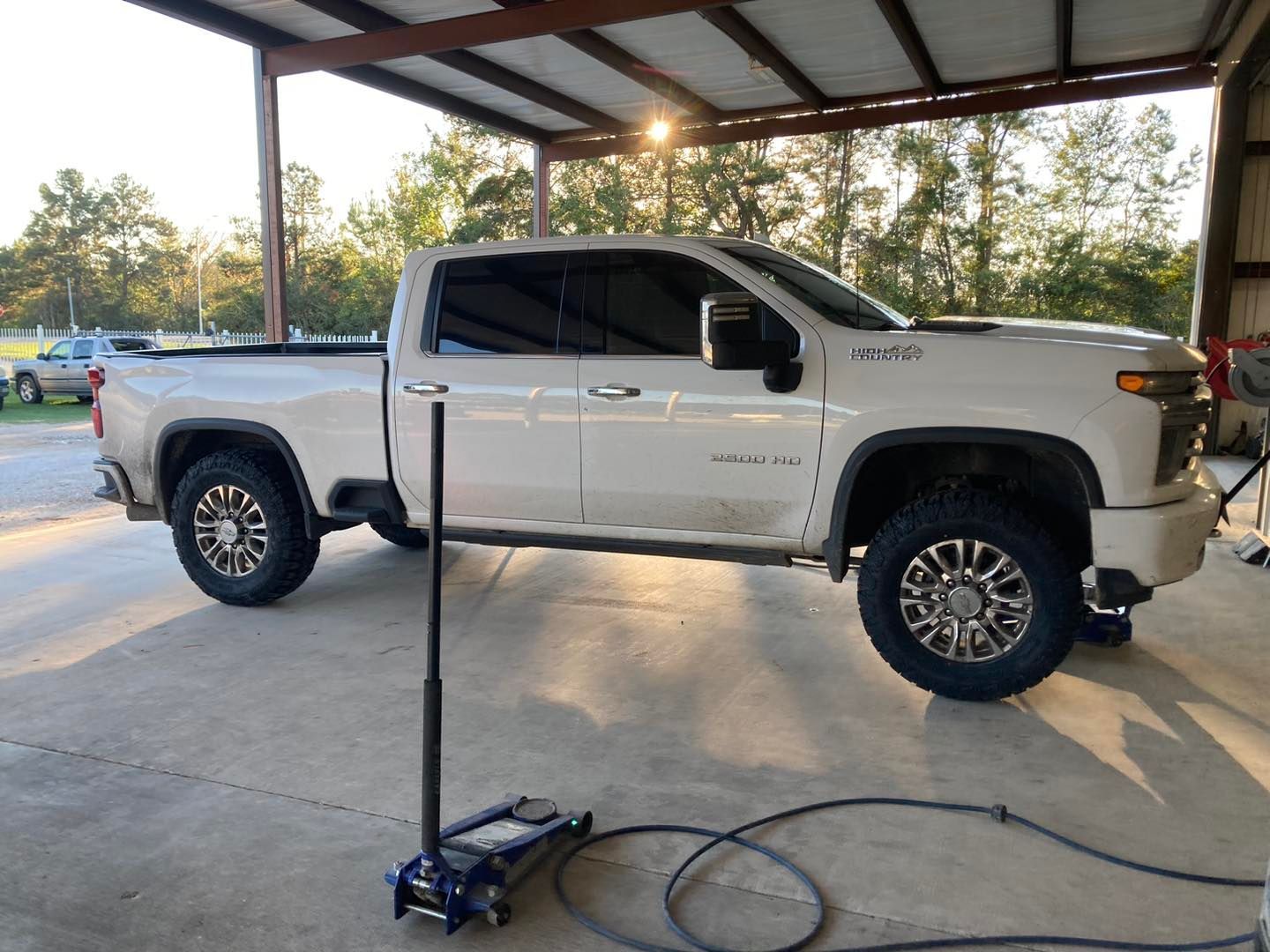 White pickup truck under a carport, with a mobile car lift in the foreground.