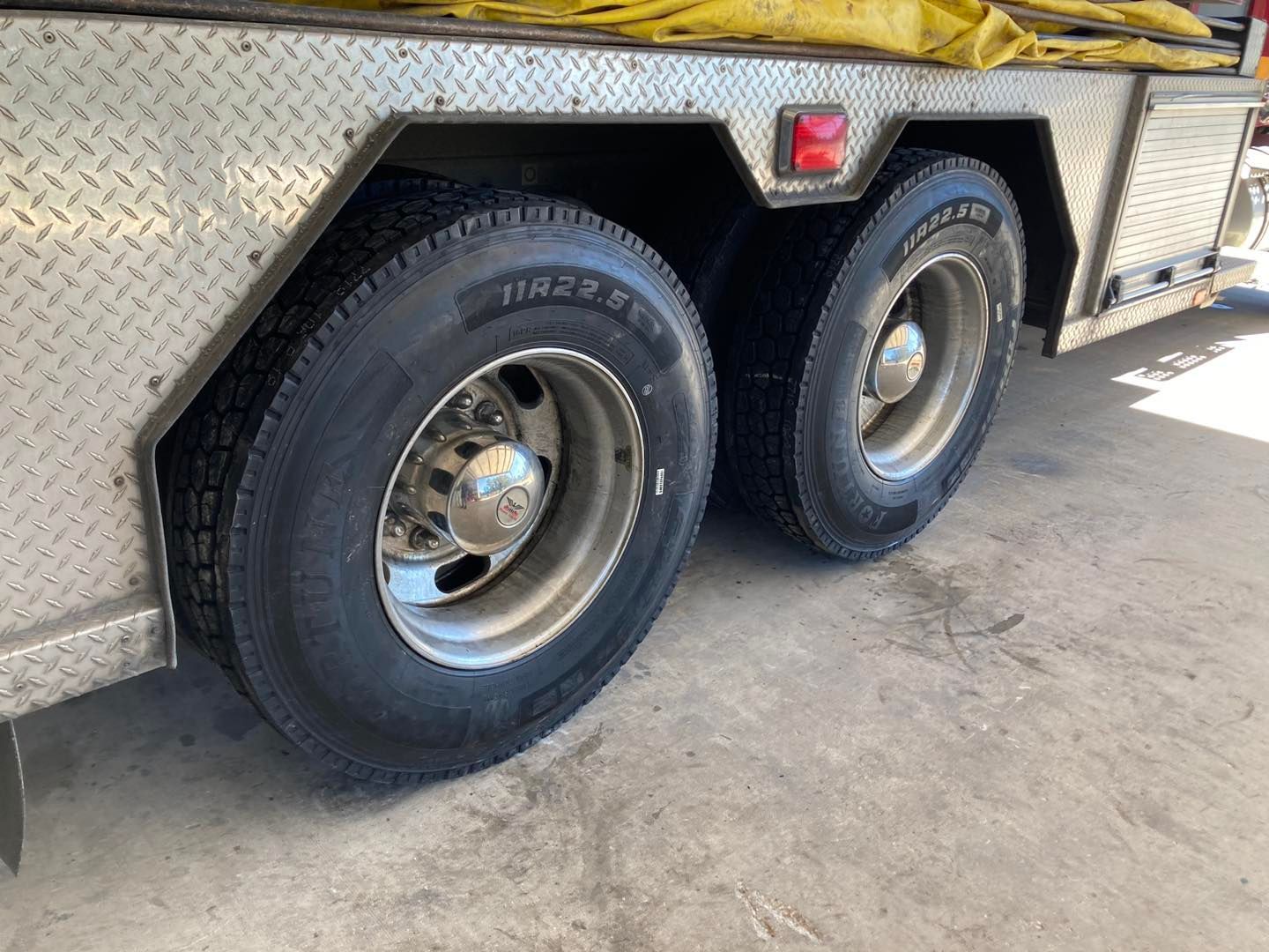 Two rear tires on a silver diamond-plate truck bed, parked on concrete, with a red marker light above.