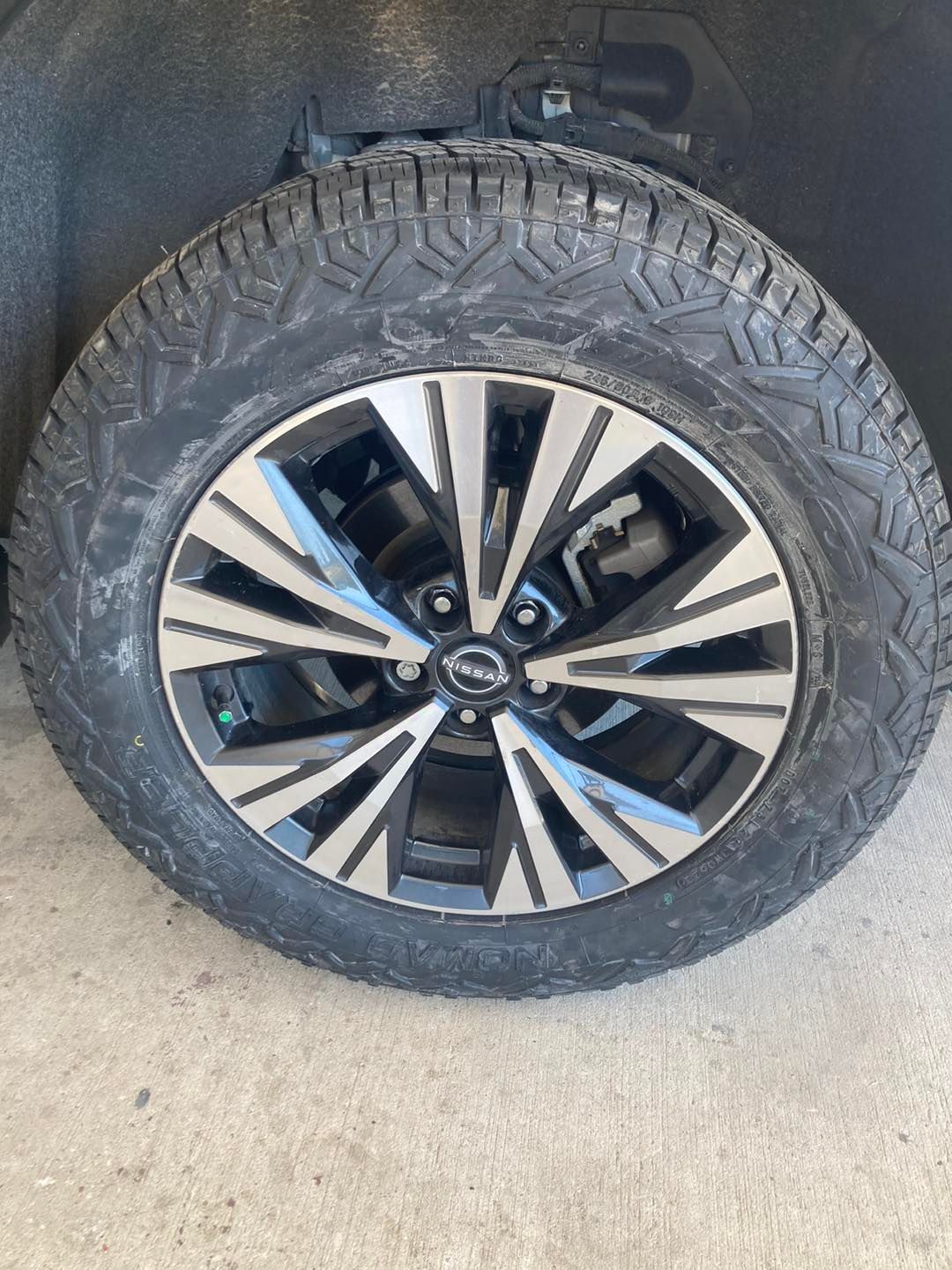 Close-up of a vehicle tire and alloy wheel with black and silver spokes on a concrete surface