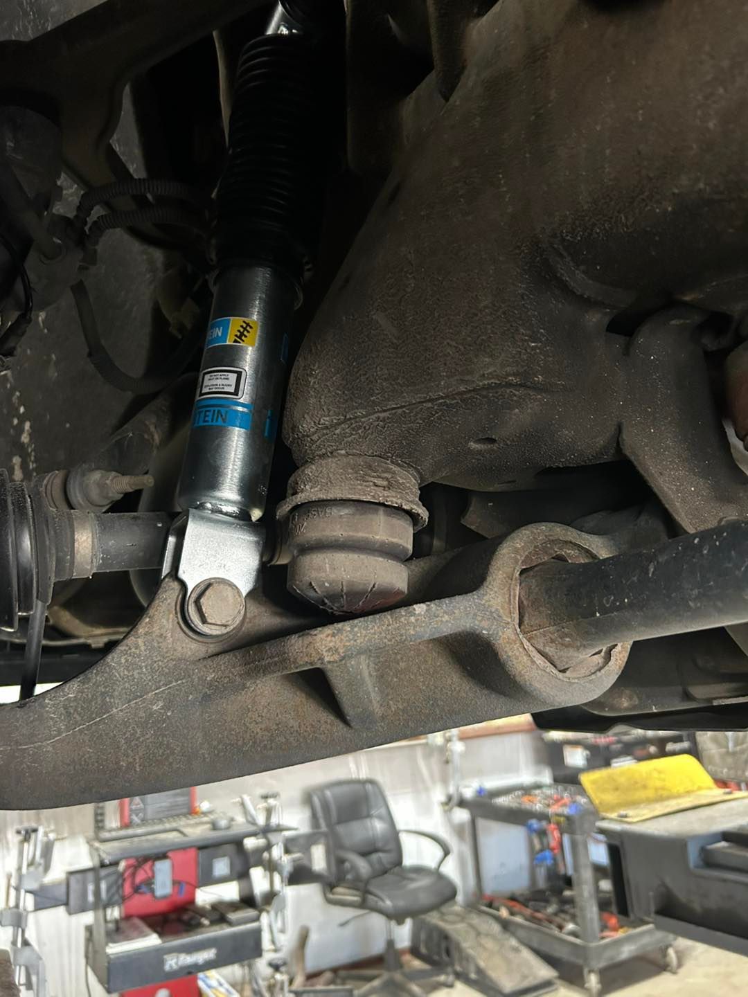 Car suspension and steering linkage close-up with black shock absorber and rusted metal components