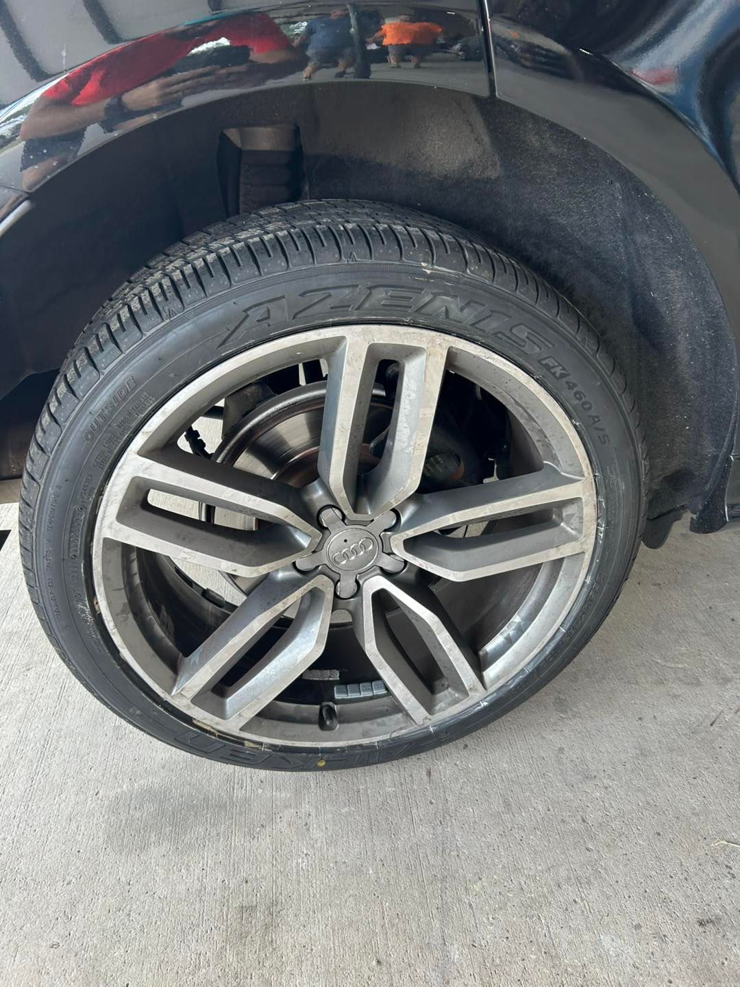 Close-up of a dusty car wheel with a damaged alloy rim and black tire on concrete.