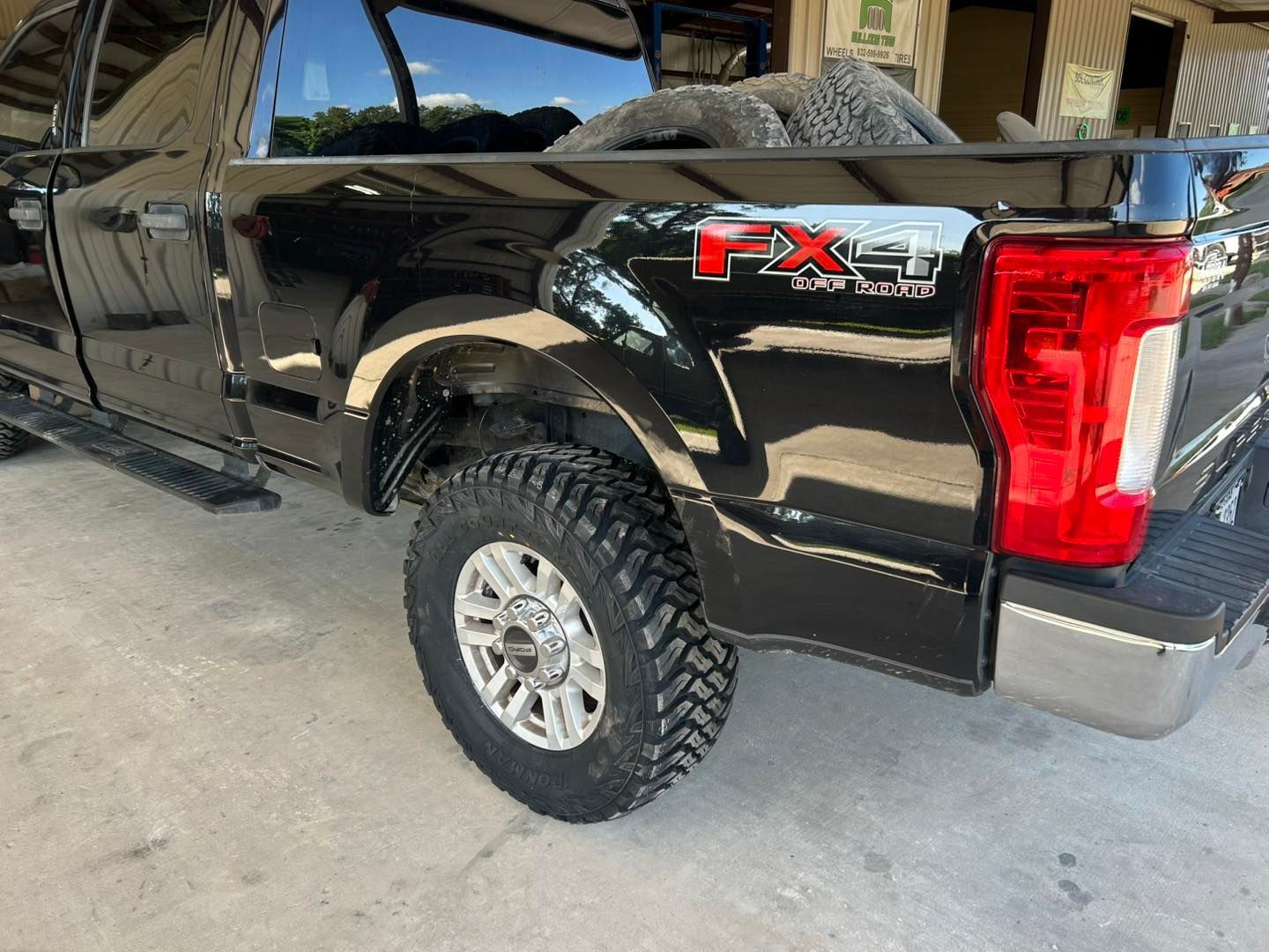 Black pickup truck rear side view with off-road tires parked in a garage.