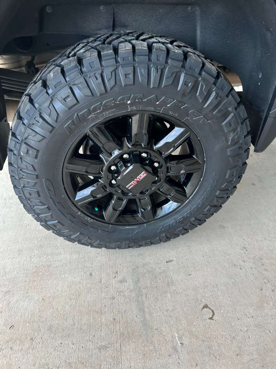 Black off-road tire and rim on a vehicle, shown close-up in a garage.
