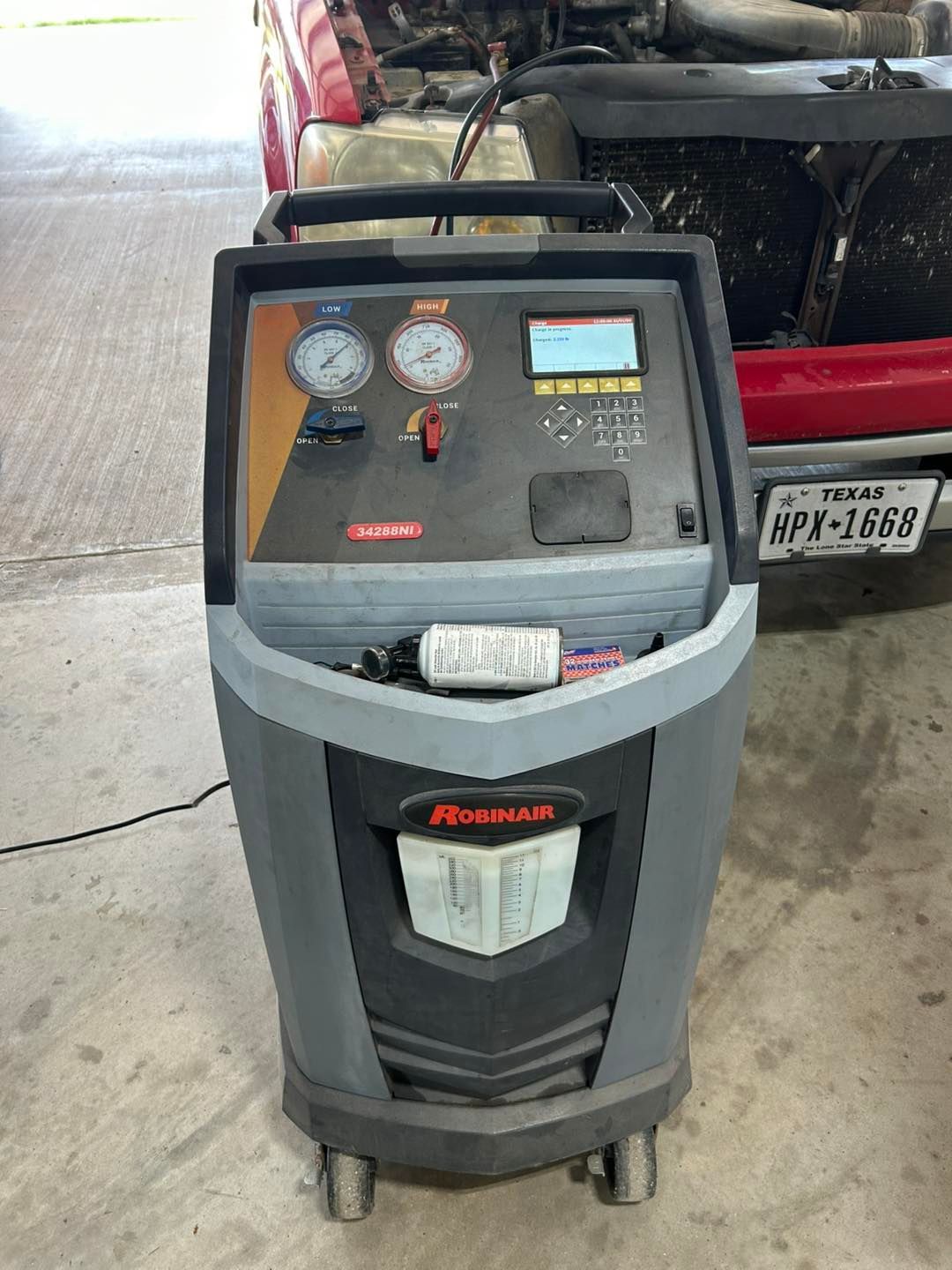Portable air conditioner on a workshop floor beside a red car, with gauges and control panel visible