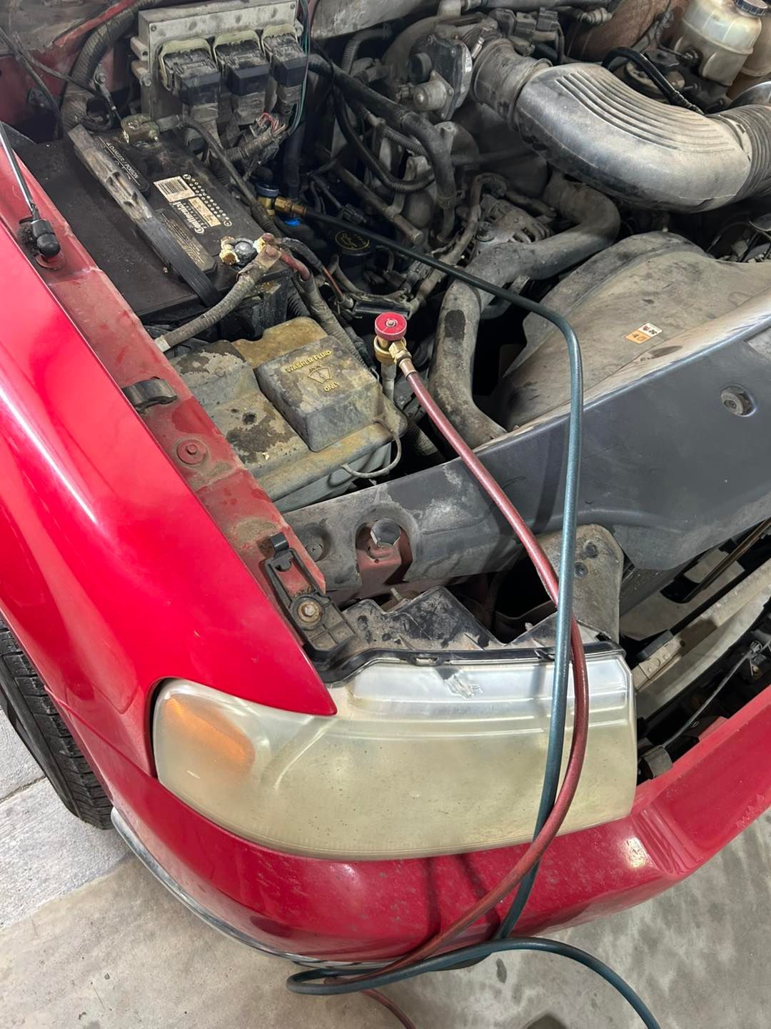 Red car with hood open, showing engine bay and a battery jump cable attached.