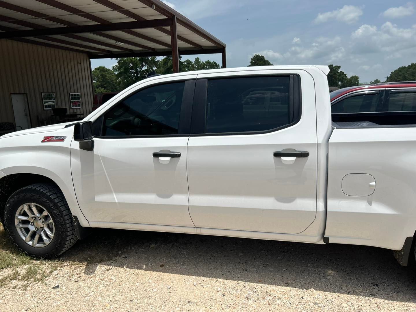White crew cab pickup truck parked beside a building on a gravel lot.