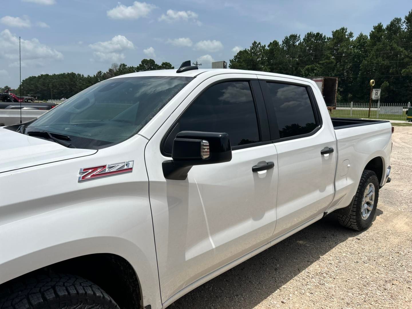 White crew cab pickup truck parked outdoors on a sunny day, side view, with tinted windows.