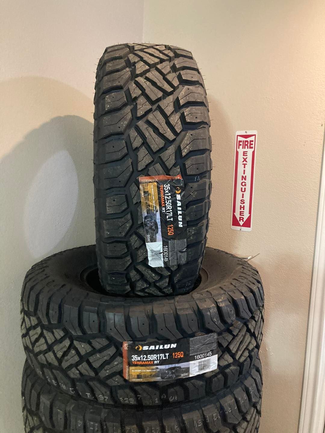 Two off-road tires stacked, one standing upright, with a red fire extinguisher sign behind them.