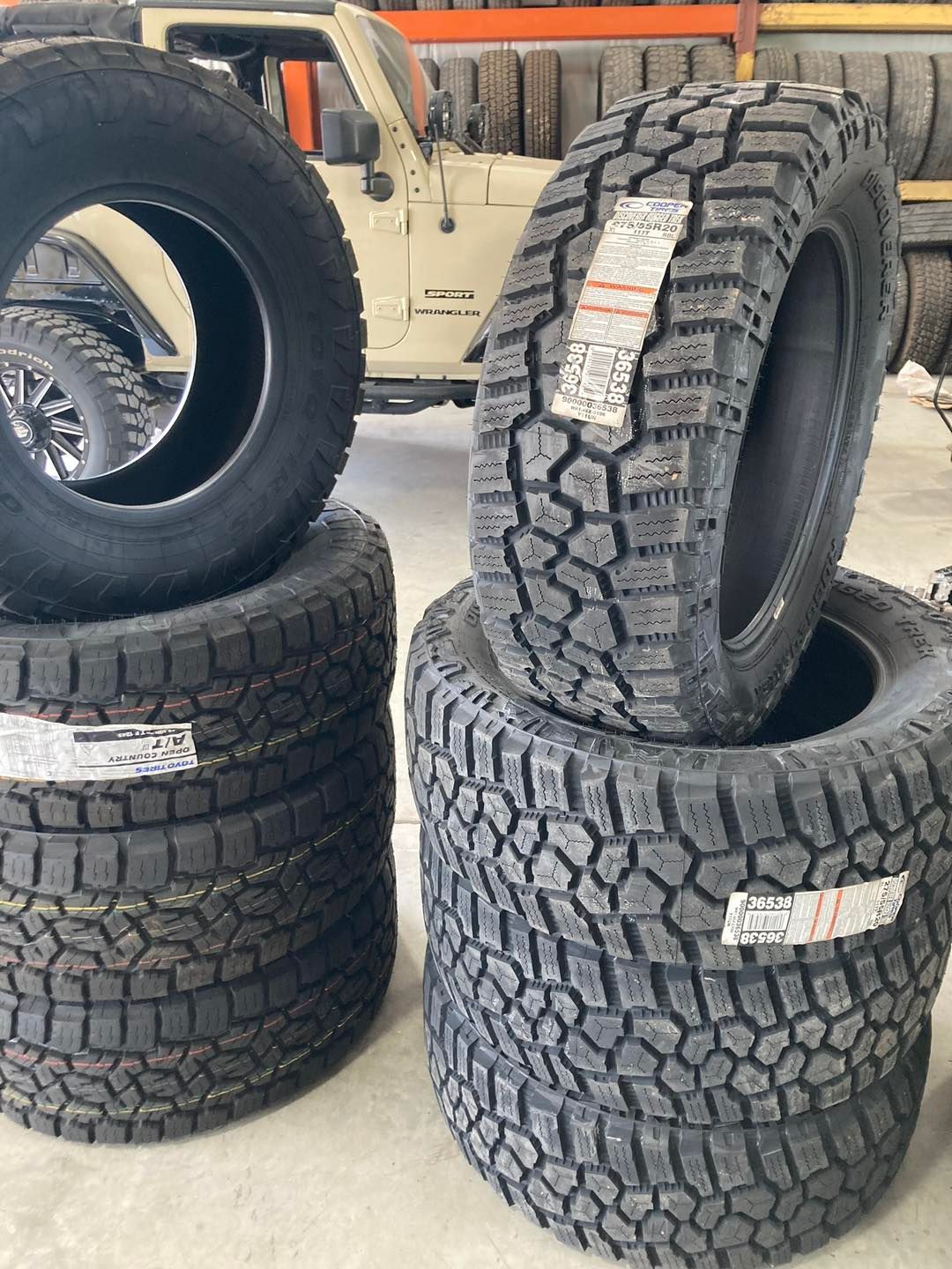 Stacks of off-road tires in a garage, with one tire leaning against a Jeep in the background.