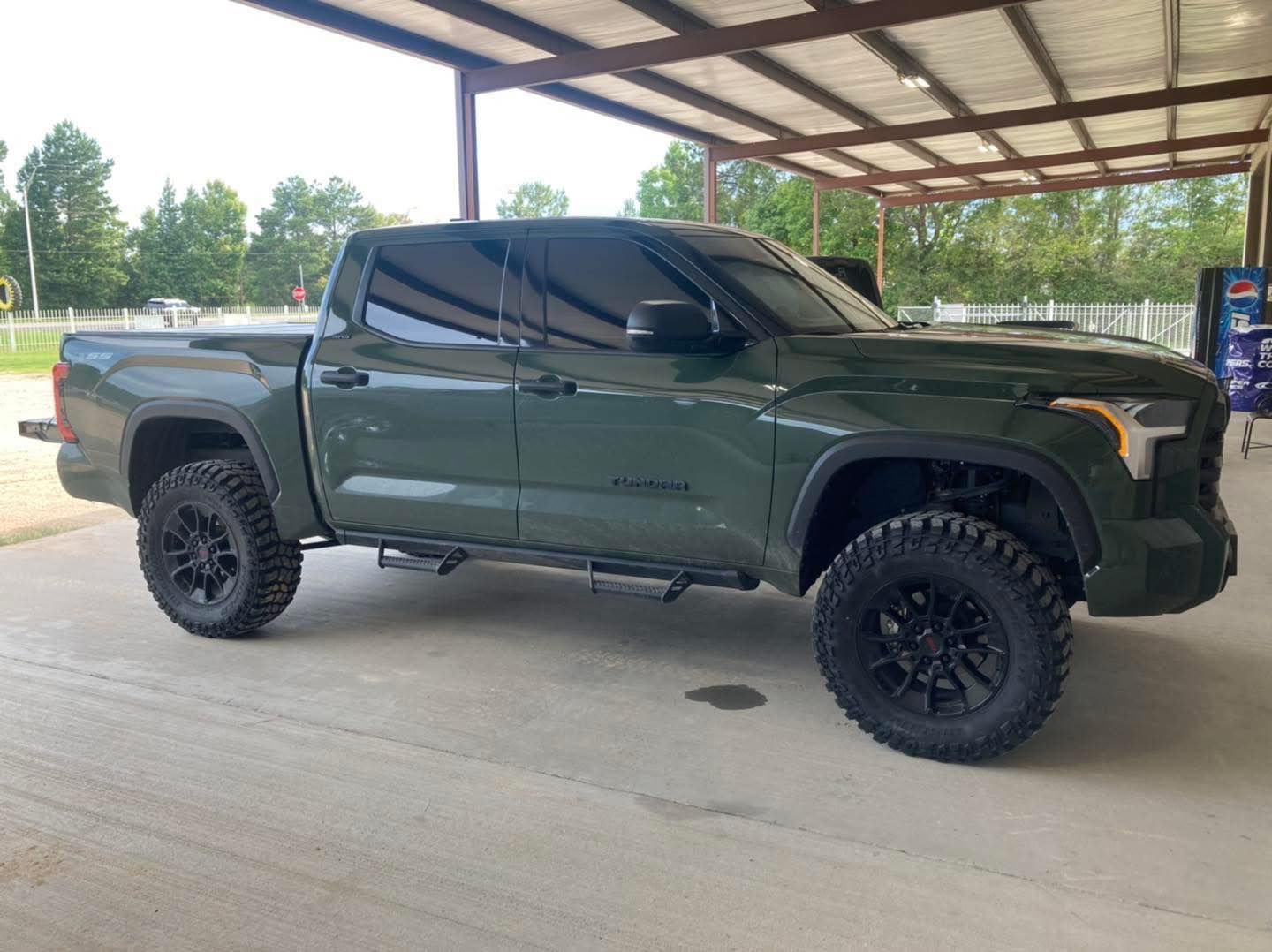 Dark green lifted pickup truck parked under a metal canopy